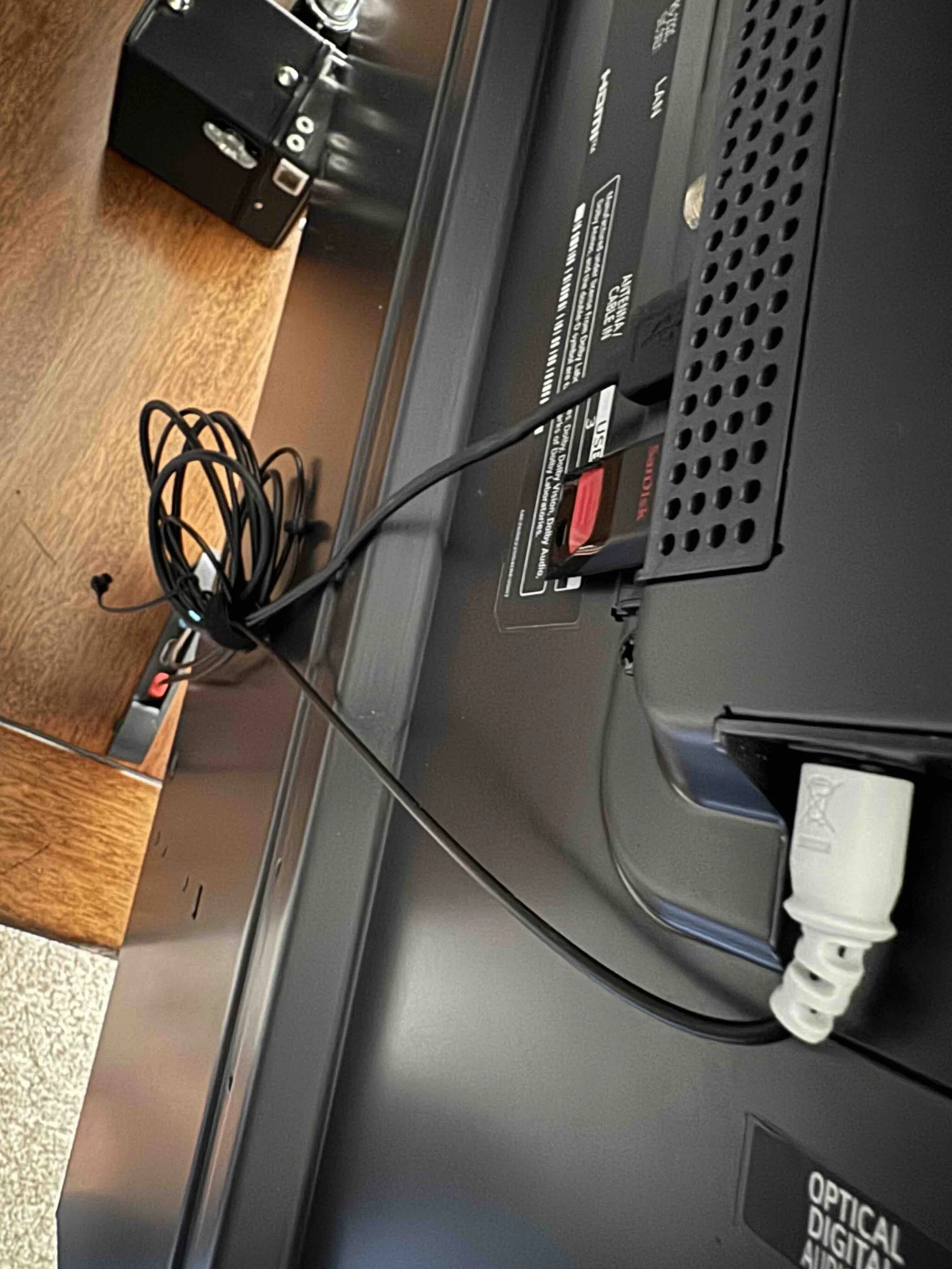 Front view of an electronic voting machine with a black body, a keypad on the right, and a small screen indicating "OPTICAL DIGIT". There is a tangled black cable connected to the machine, placed on a wooden surface.