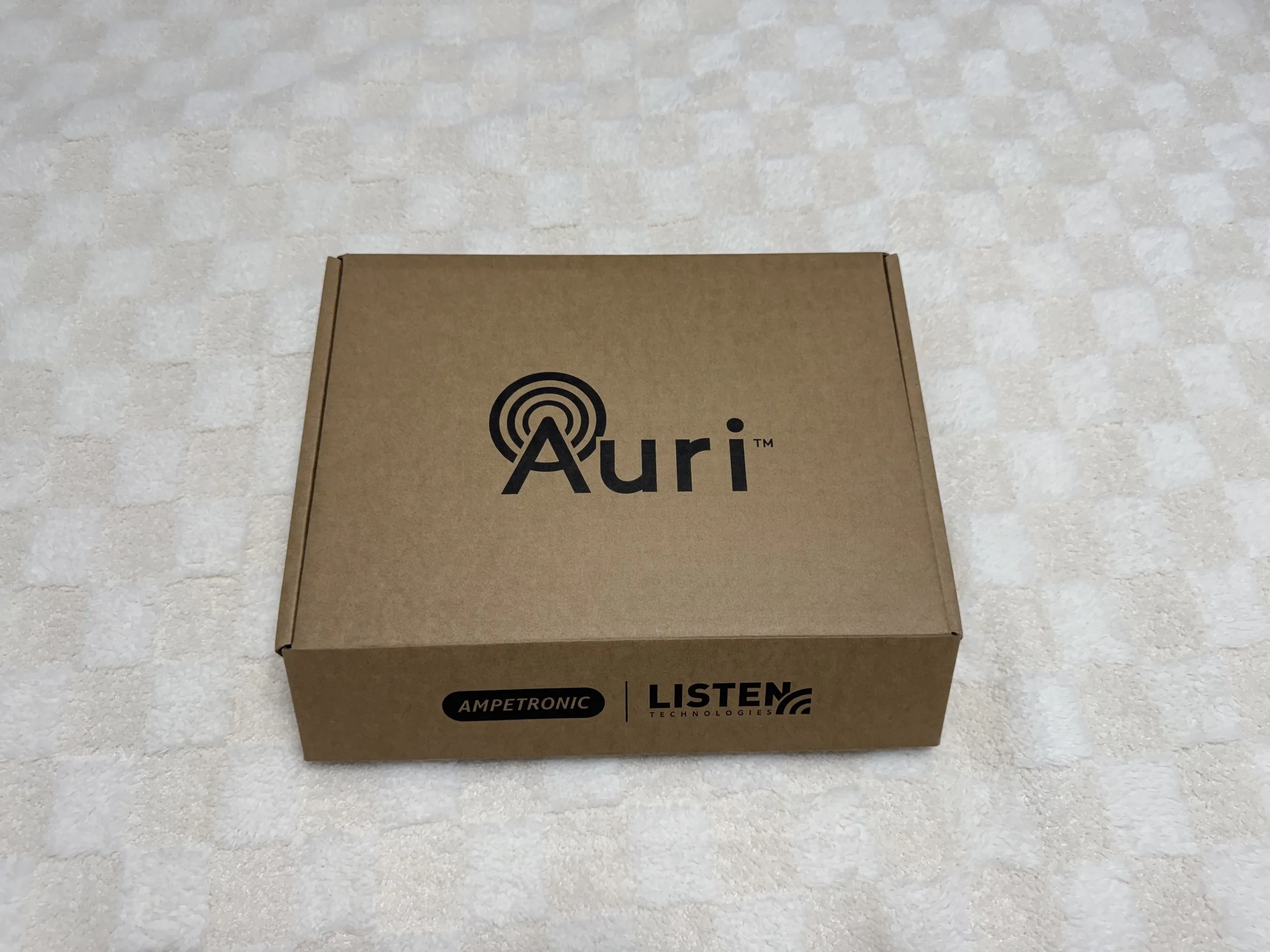 A brown cardboard box with black logos and text, placed on a white tiled surface.
