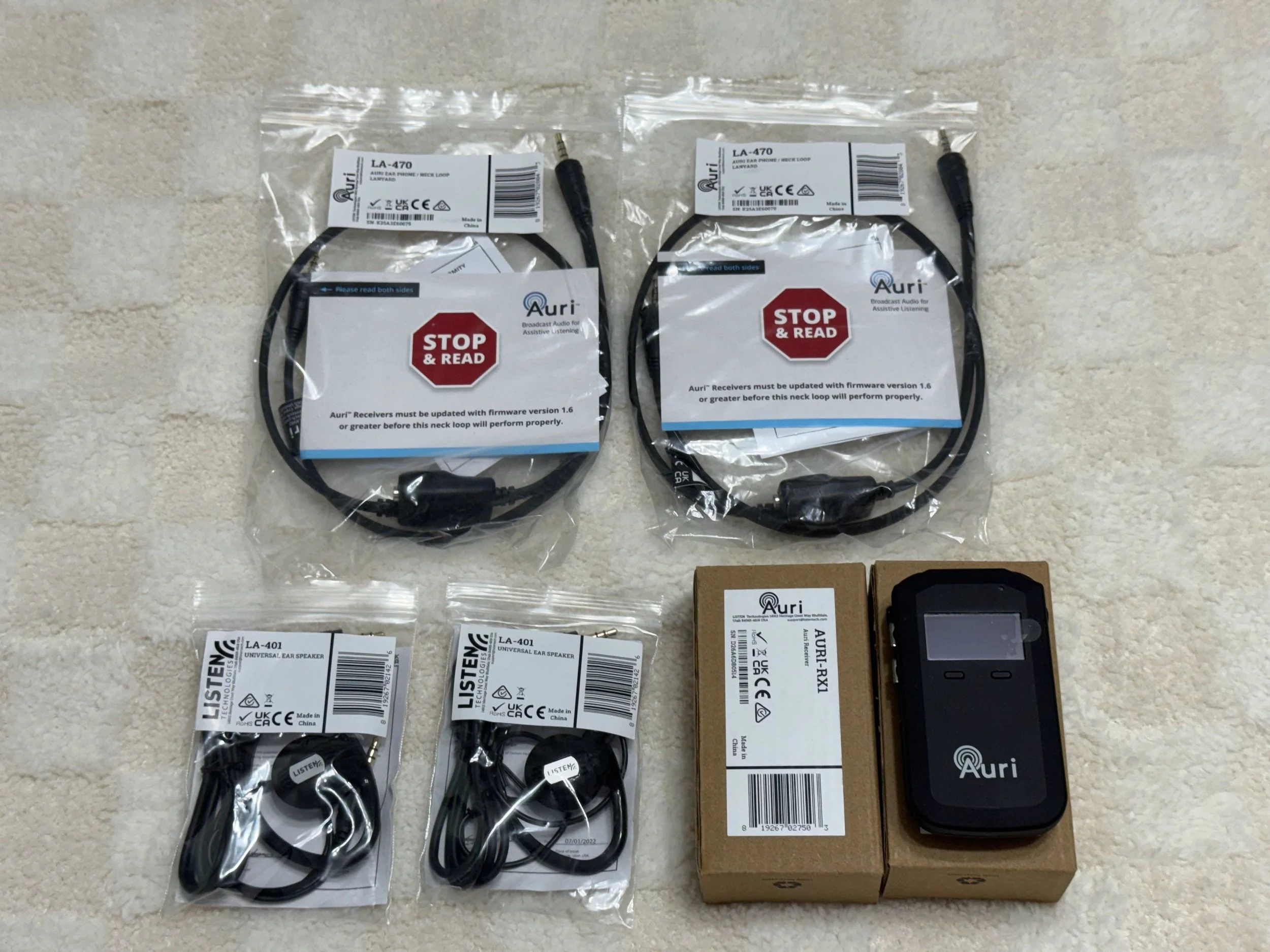 Two packages of black ear microphone cords labeled Auri LA-470, along with several smaller packages of other electronic components and a digital device, all placed on a light-colored surface.