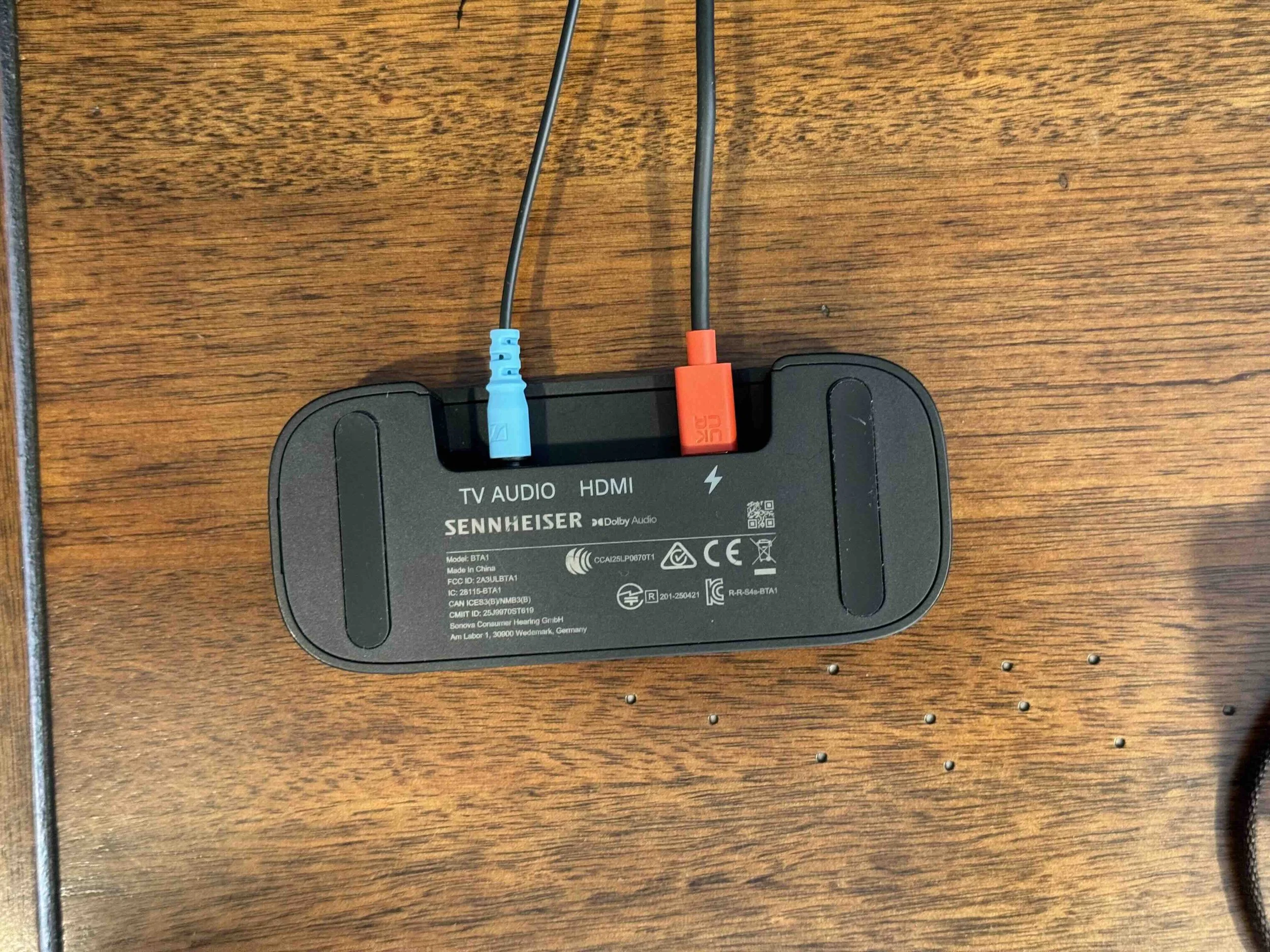 A black device labeled Sennheiser with two colored cables inserted into ports, placed on a wooden surface.