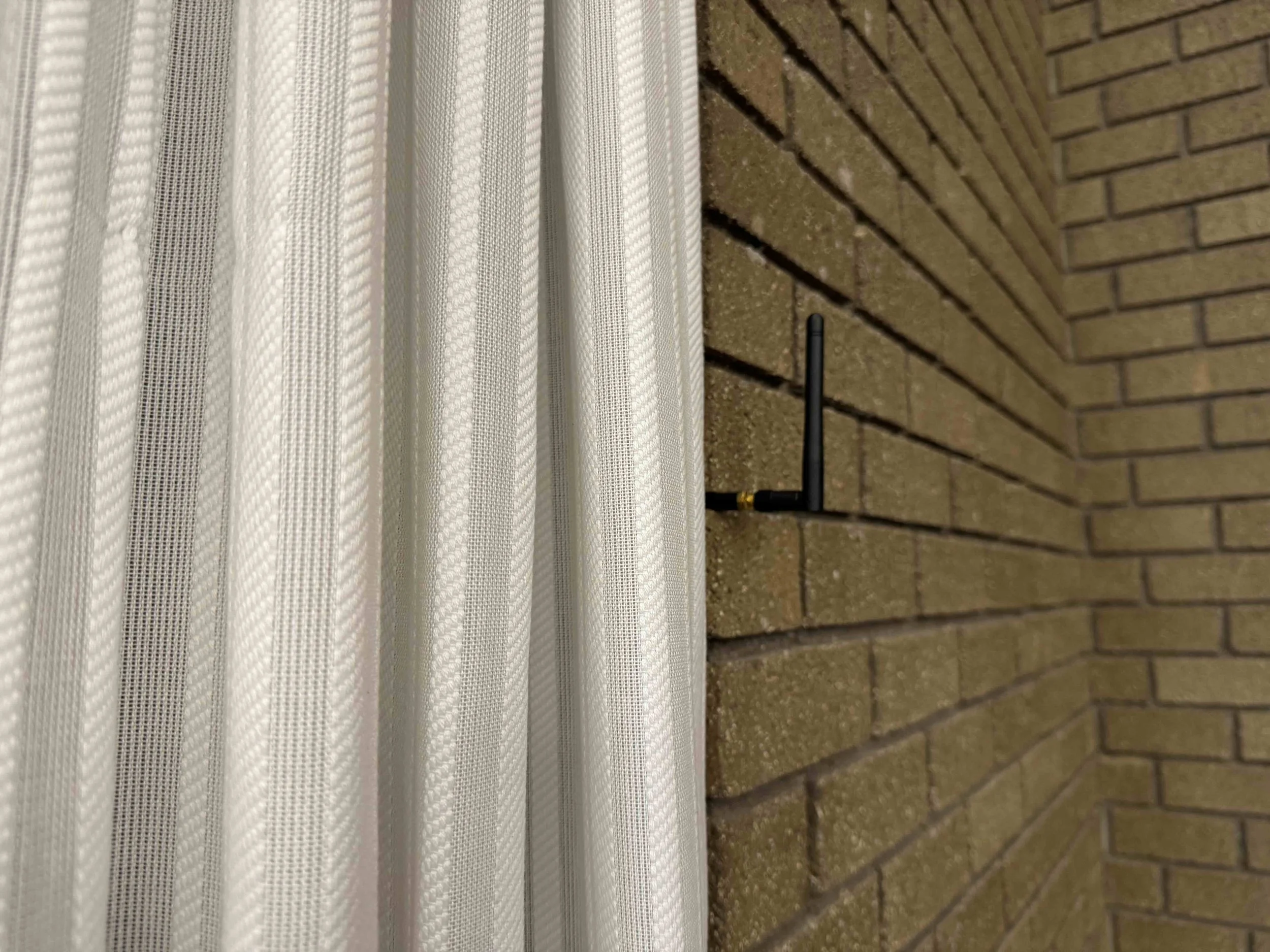 Close-up of white vertical blinds next to a brown brick wall with a small black wire.