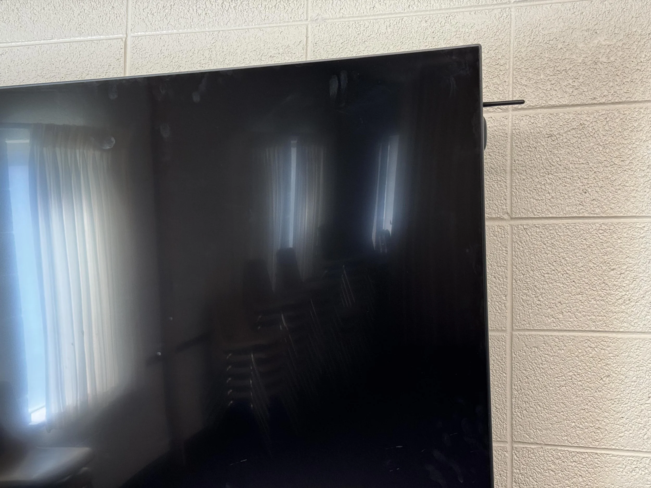 Close-up of a computer monitor with a black screen against a beige cinder block wall.