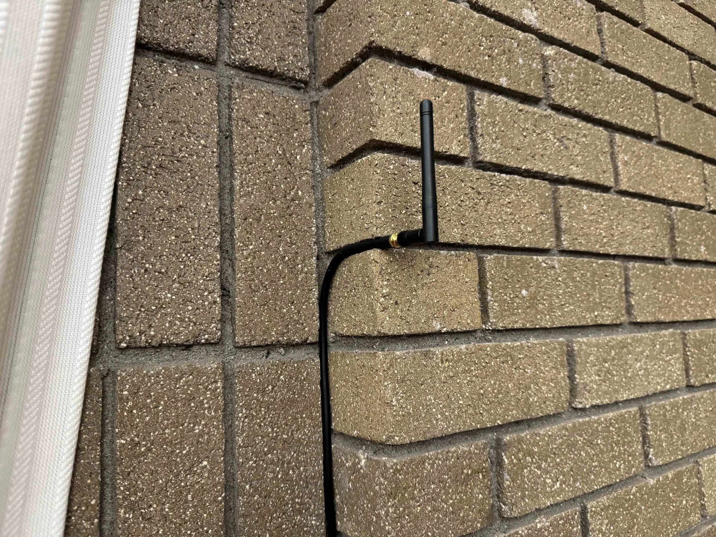 A black Wi-Fi antenna leaning against a brick wall.