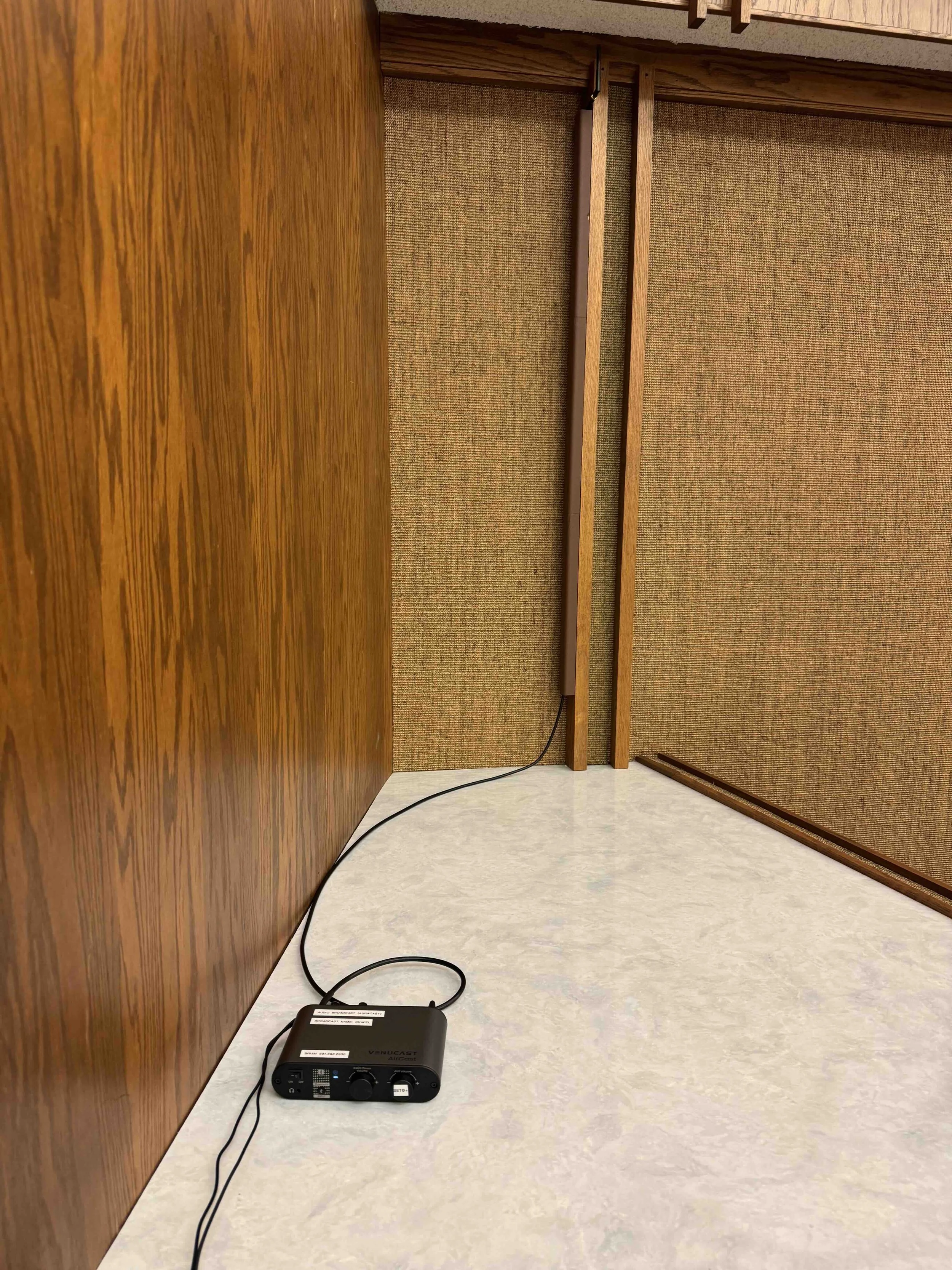 A black microphone connected to a black audio receiver on a beige countertop, with wooden and fabric-covered partitions in the background.
