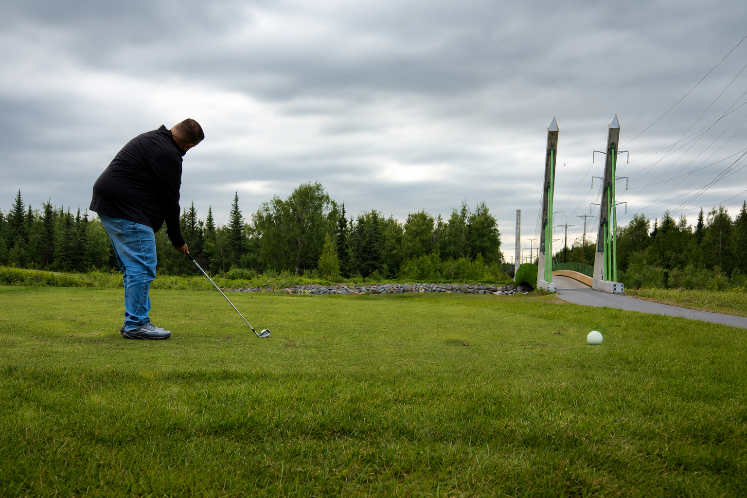 Golfer hitting an iron shot on a Minnesota golf course under an overcast sky.