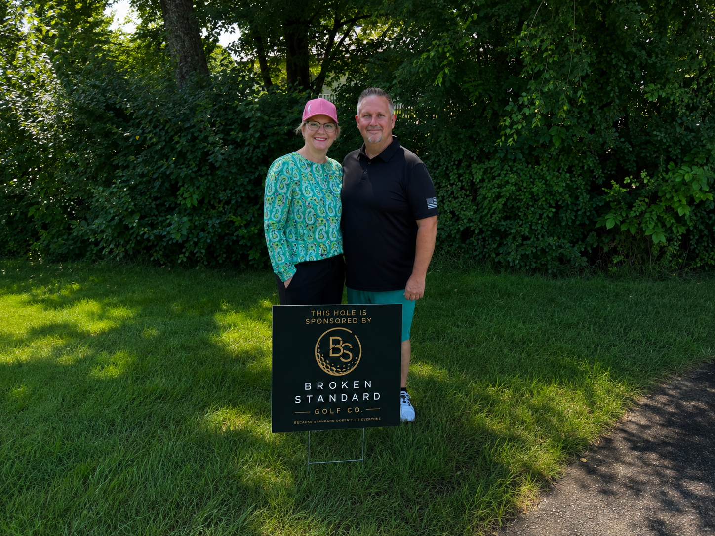 Jason and Shannon, the people behind Broken Standard Golf Co., standing with a Broken Standard Golf Co. sign.
