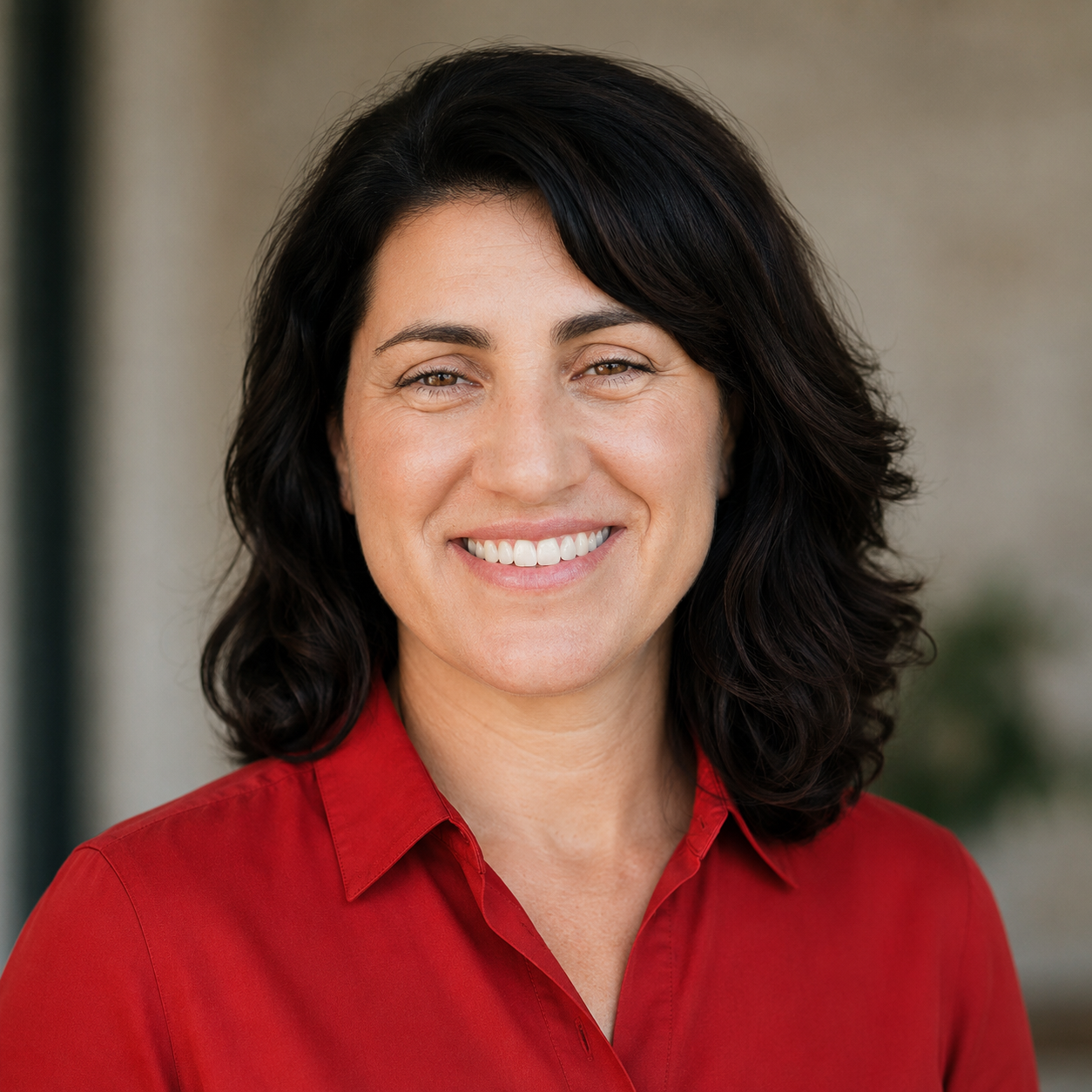 A woman with shoulder-length dark hair and a big smile, wearing a red collared shirt, standing outdoors.