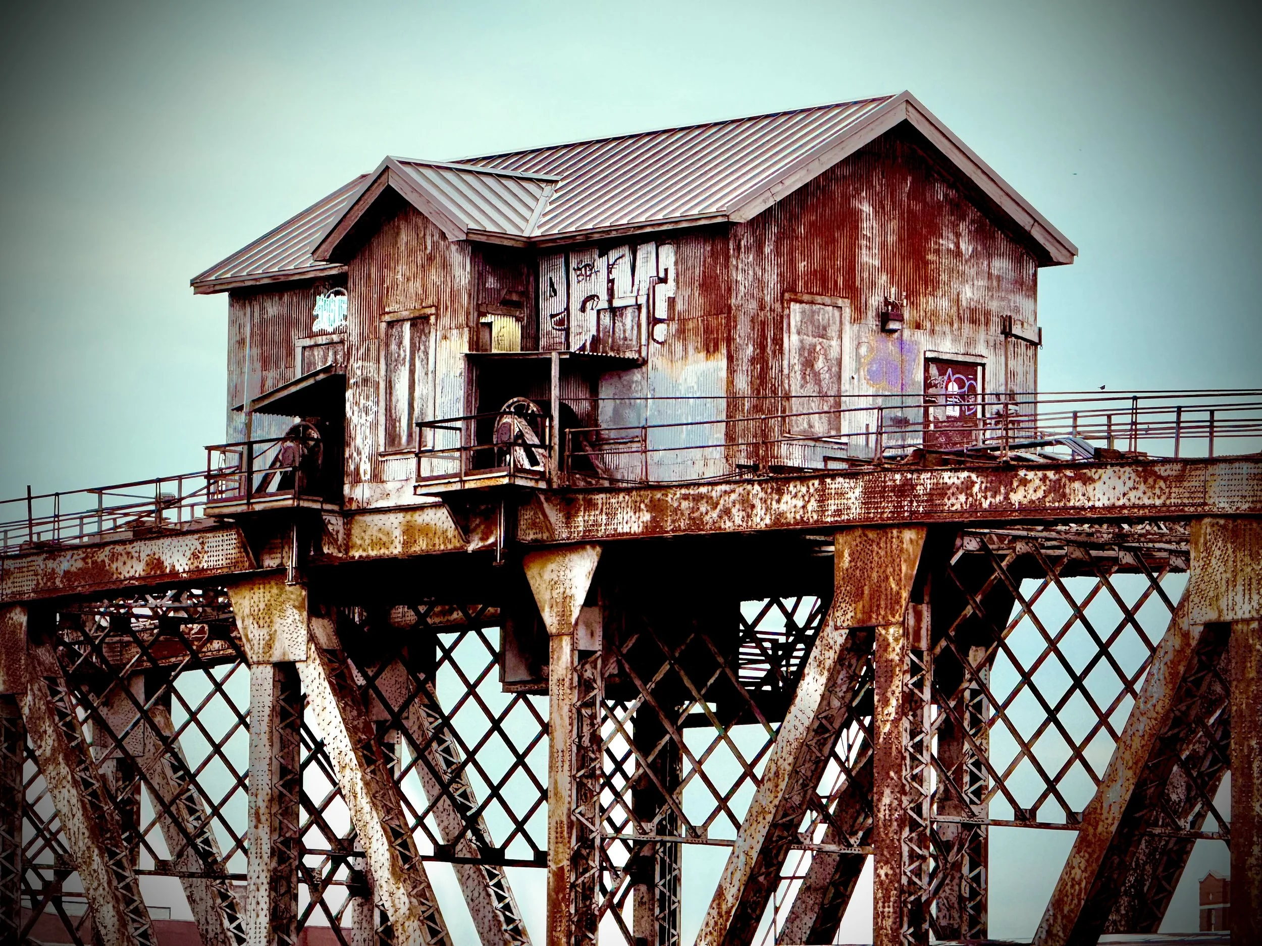 Rusted corrugated-metal building with peeling paint and graffiti on a weathered steel trestle