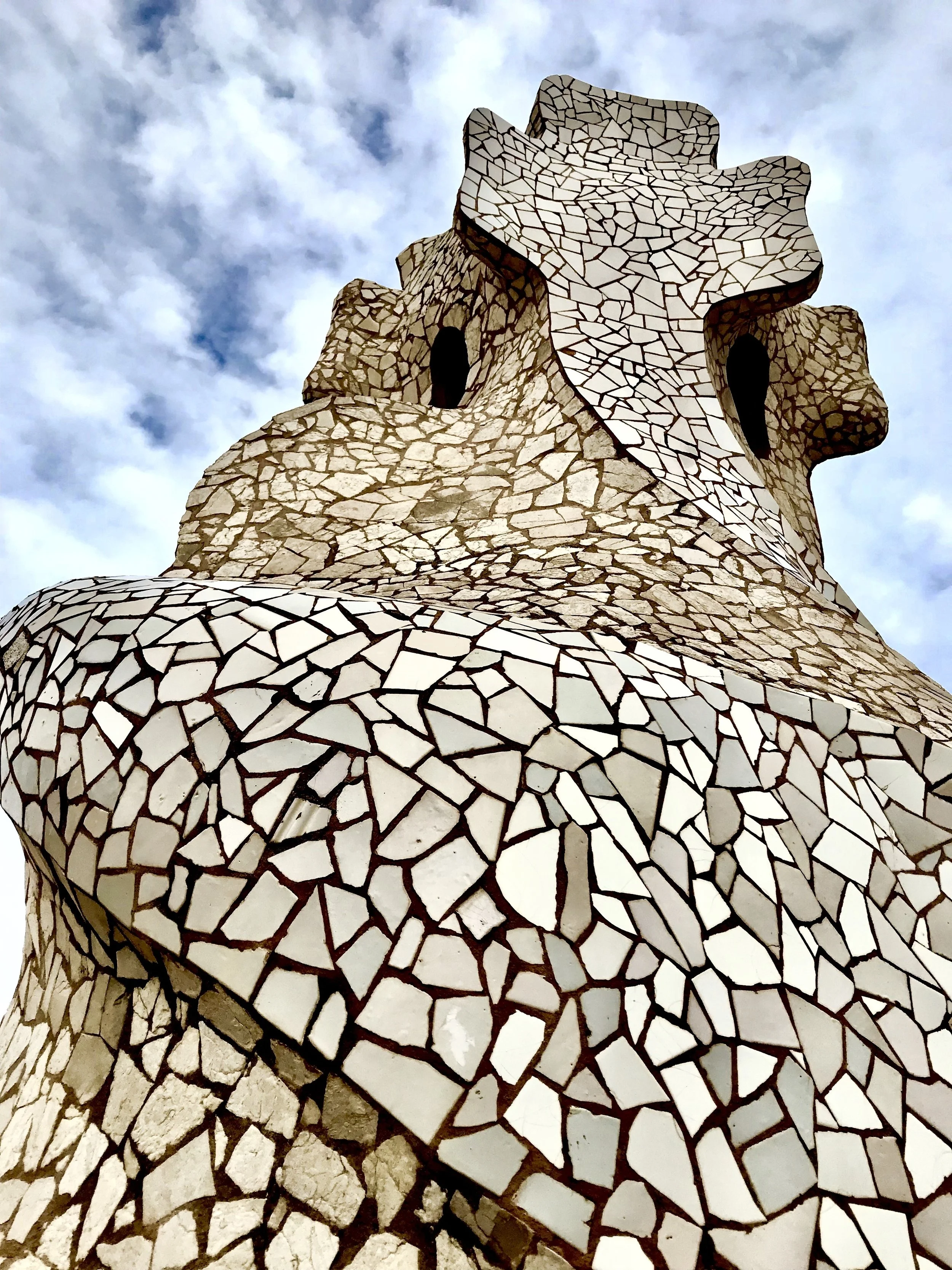 Antoni Gaudi rooftop chimney covered in white broken-tile mosaic against a cloudy sky