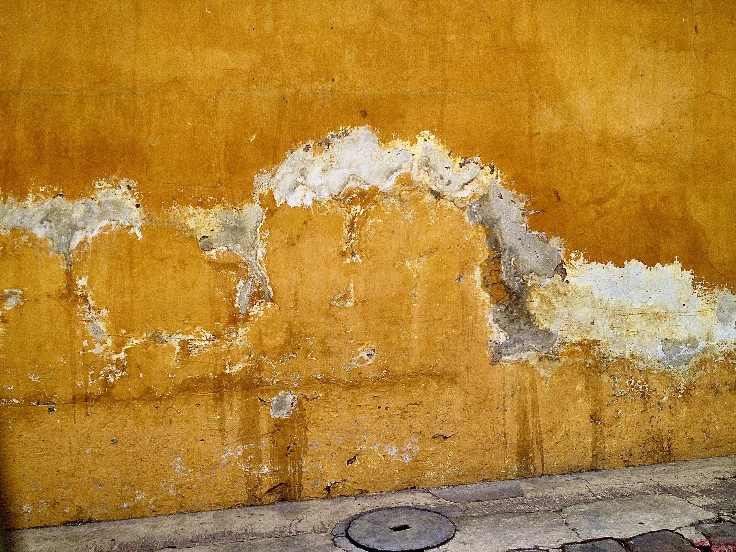 Weathered ochre wall in Antigua, Guatemala, with peeling plaster in white and gray patches
