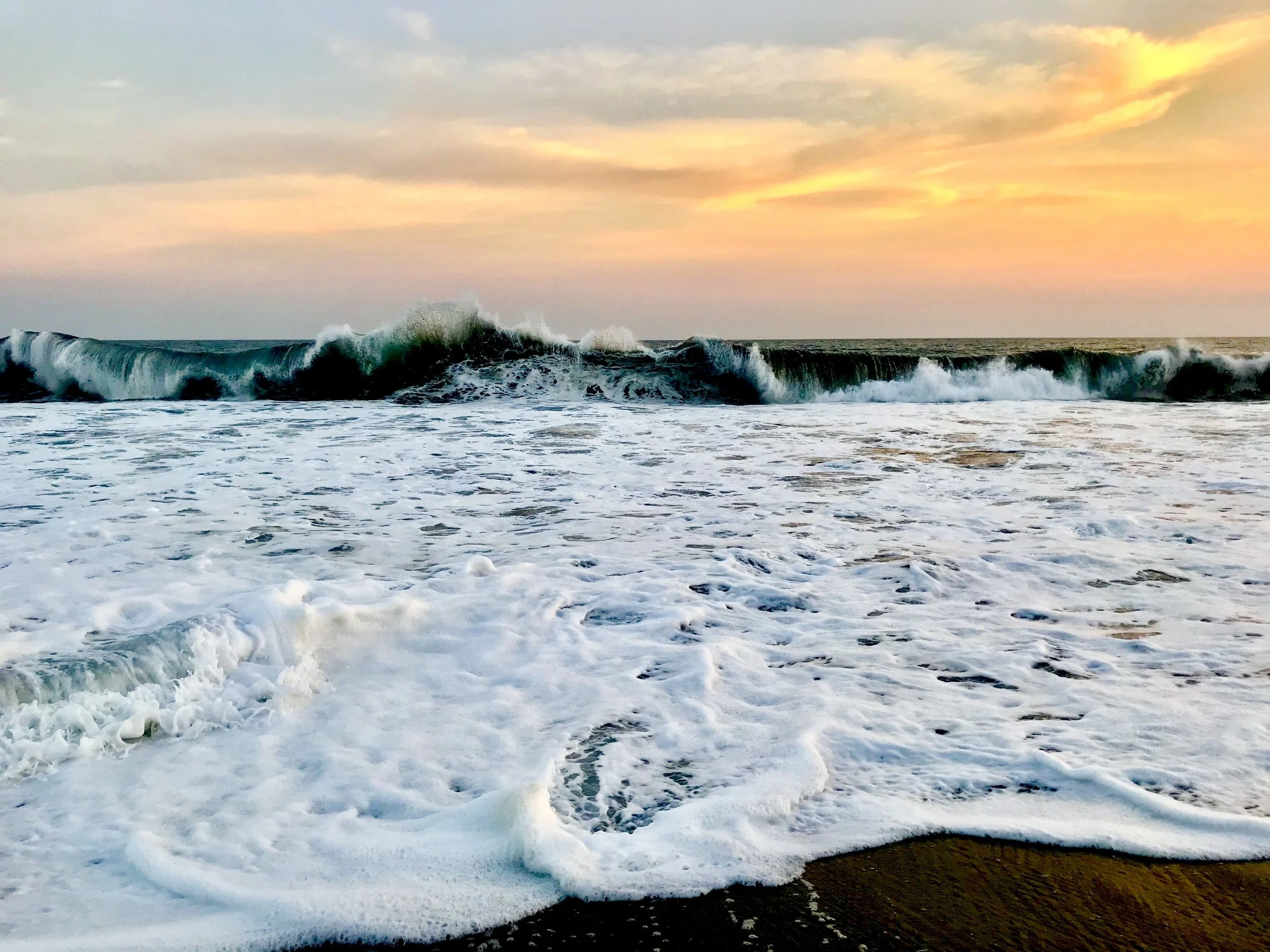 White wave foam spreading over dark volcanic sand at sunset in Monterrico, Guatemala — the ocean that inspires Susan Brady's art