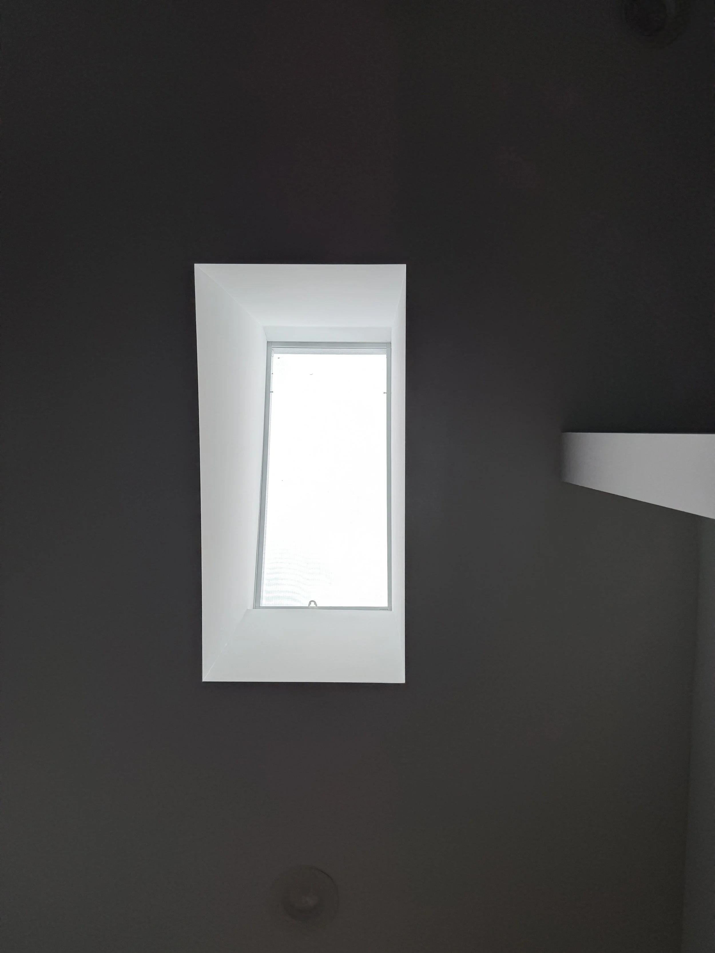 A rectangular skylight on a dark ceiling, with natural light coming through.