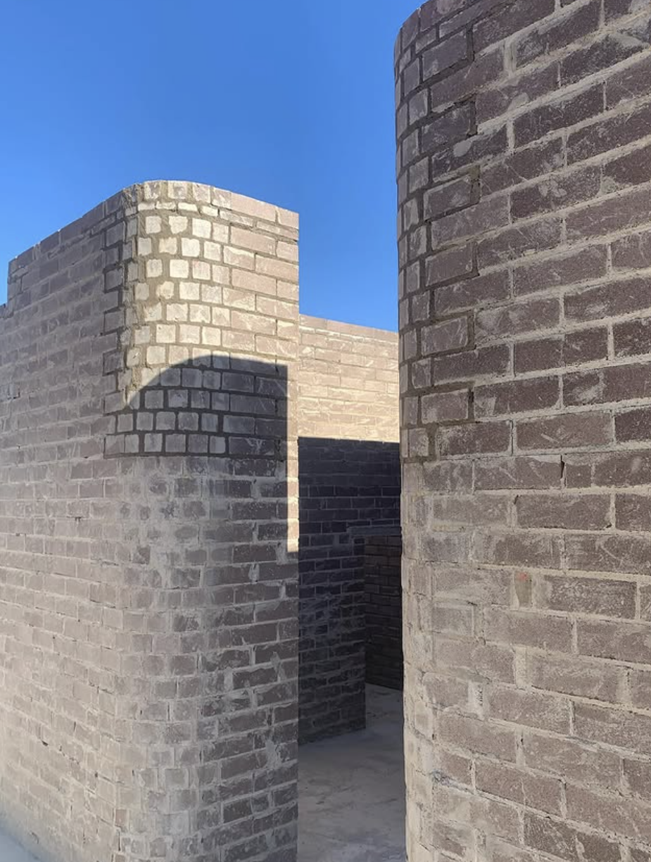 Several brick walls with shadows cast on them, under a clear blue sky.
