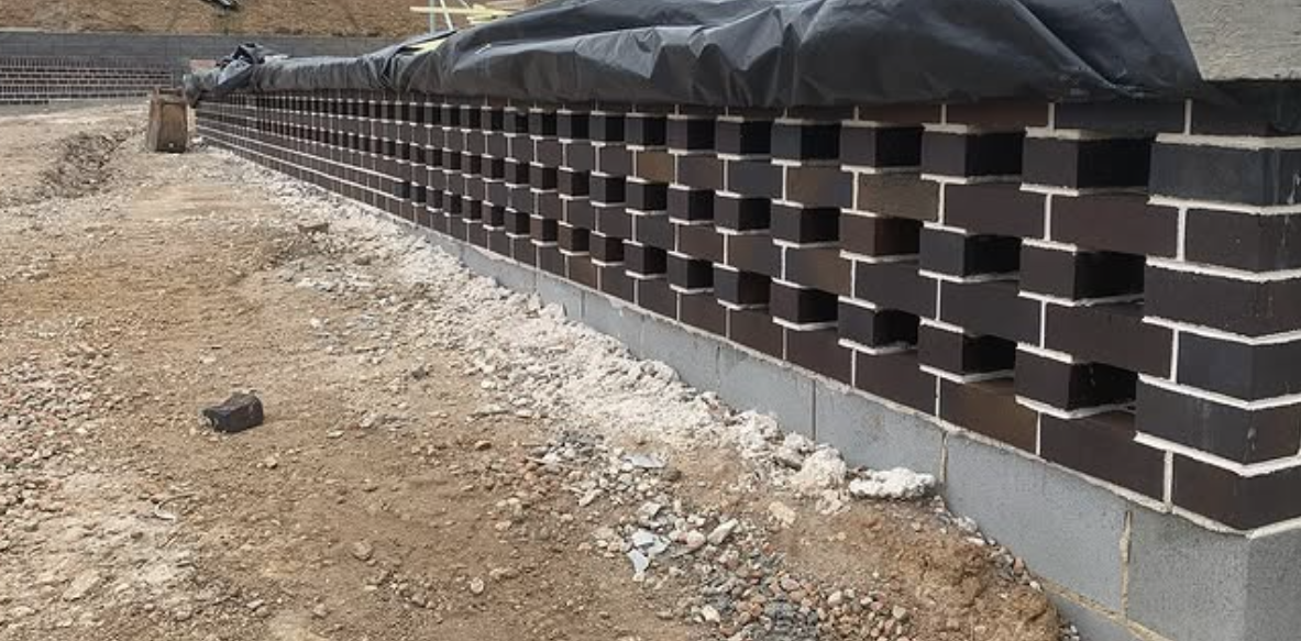 A growing brick wall construction on a building foundation, with a black insulation or waterproofing layer on top.
