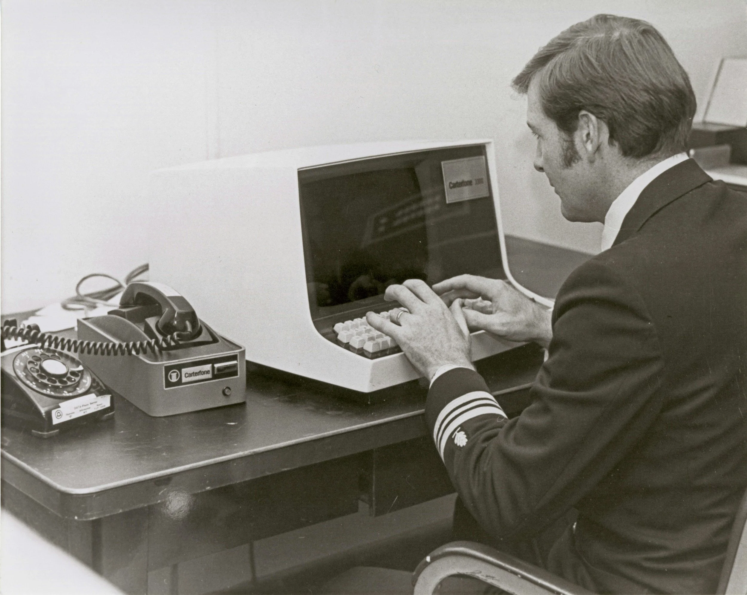 A man wearing a suit and tie sitting at a desk and using an old computer