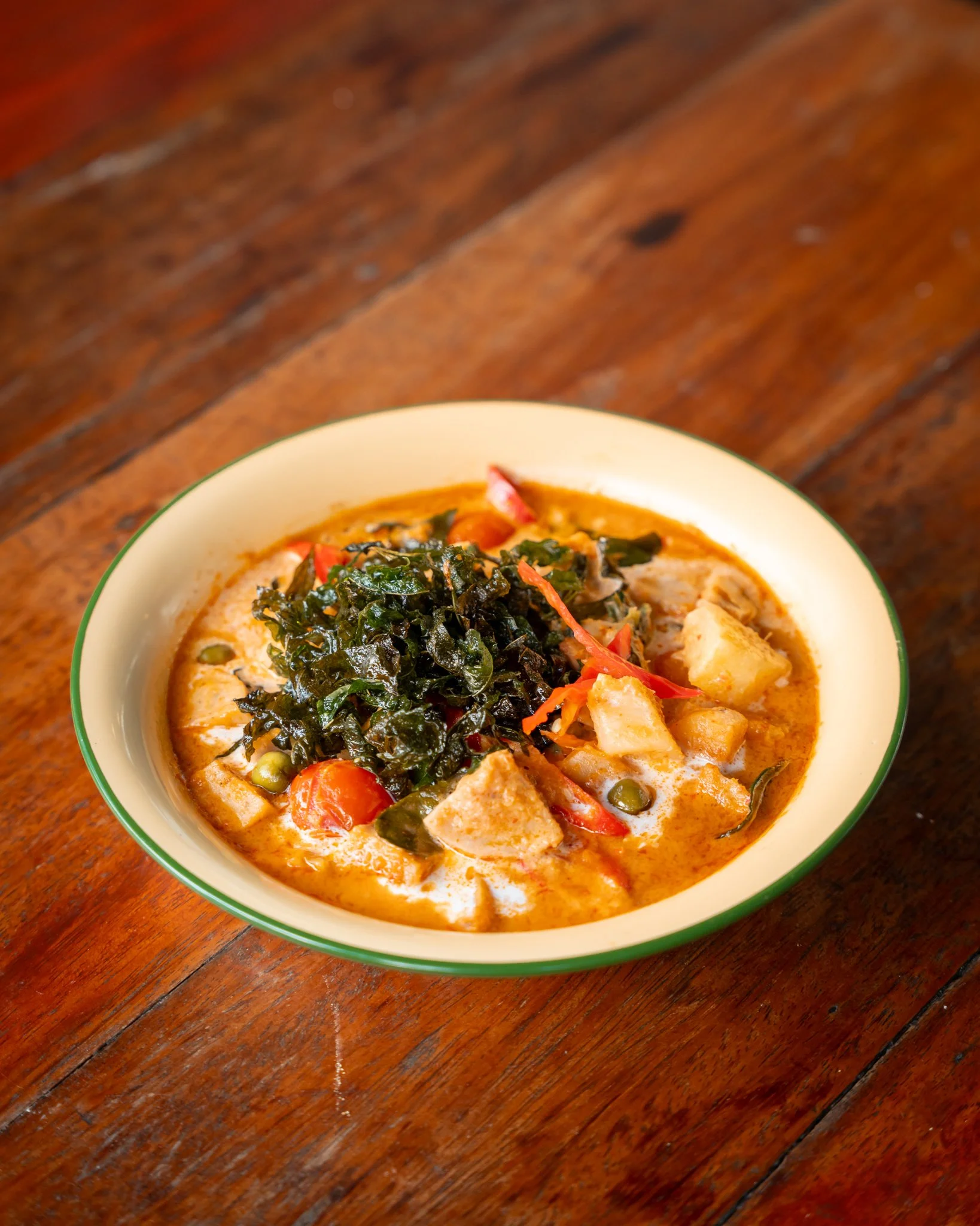 A bowl of creamy soup with vegetables and herbs on a wooden table.