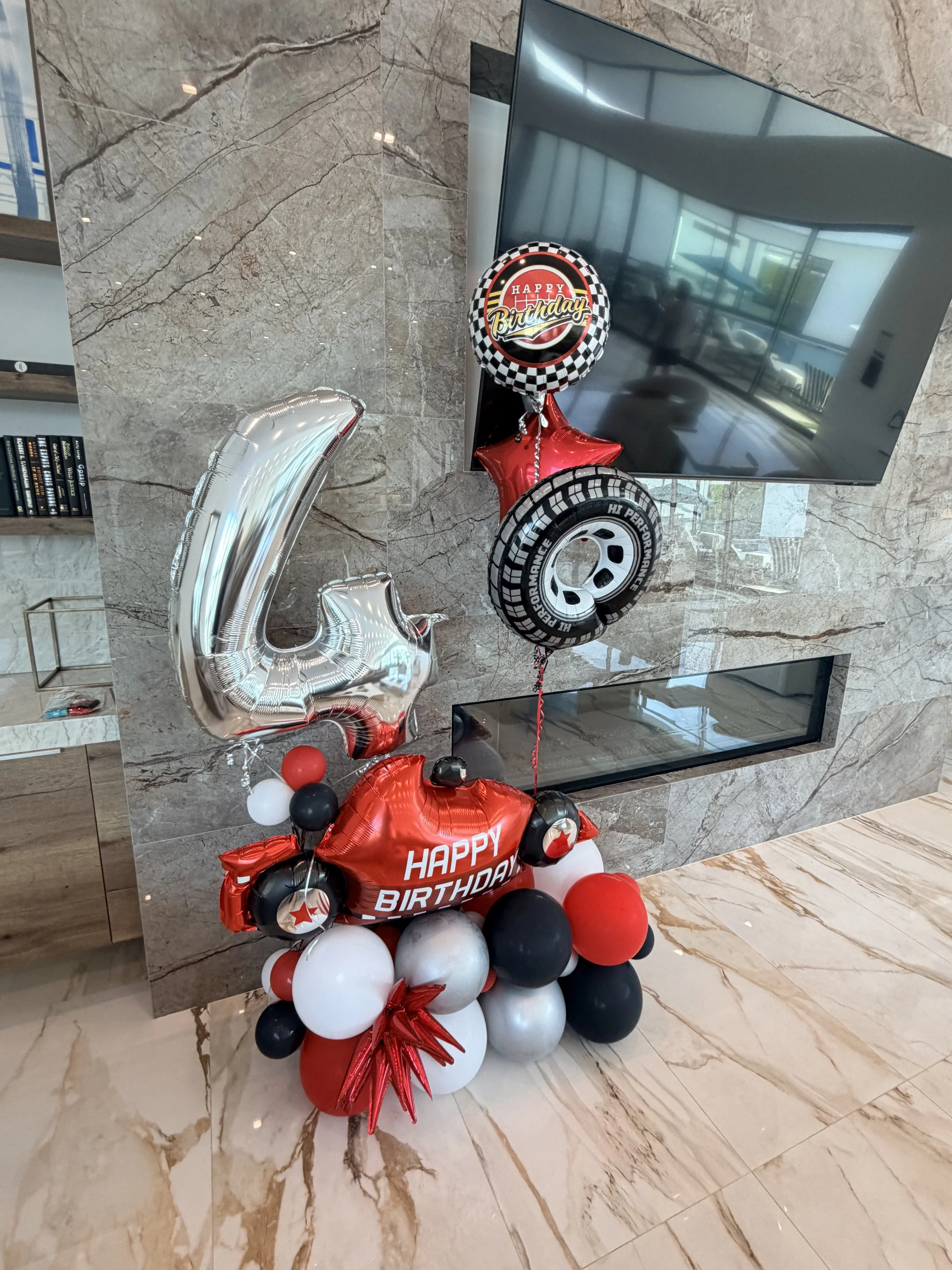 A balloon cluster with a red racecar balloon and a silver number four mylar balloon next to a marble fireplace