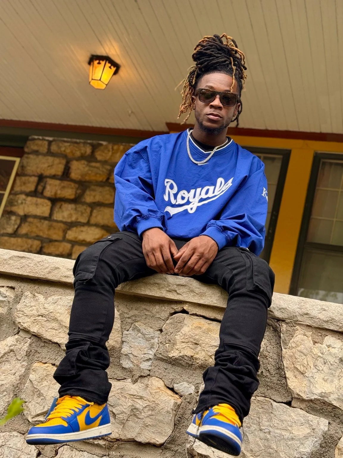 Seated fashion portrait in a blue outfit with yellow and blue sneakers.