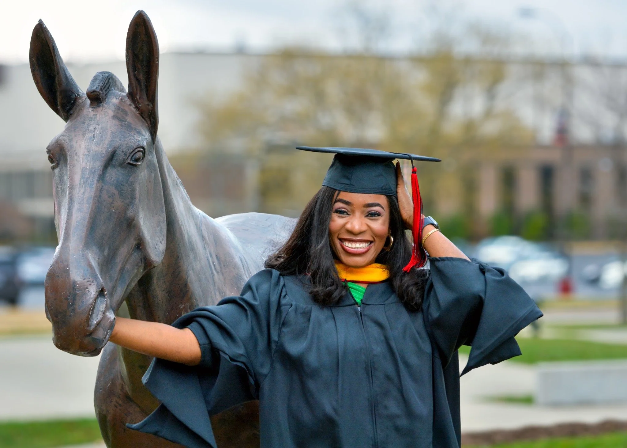Graduation portrait beside a bronze horse sculpture.