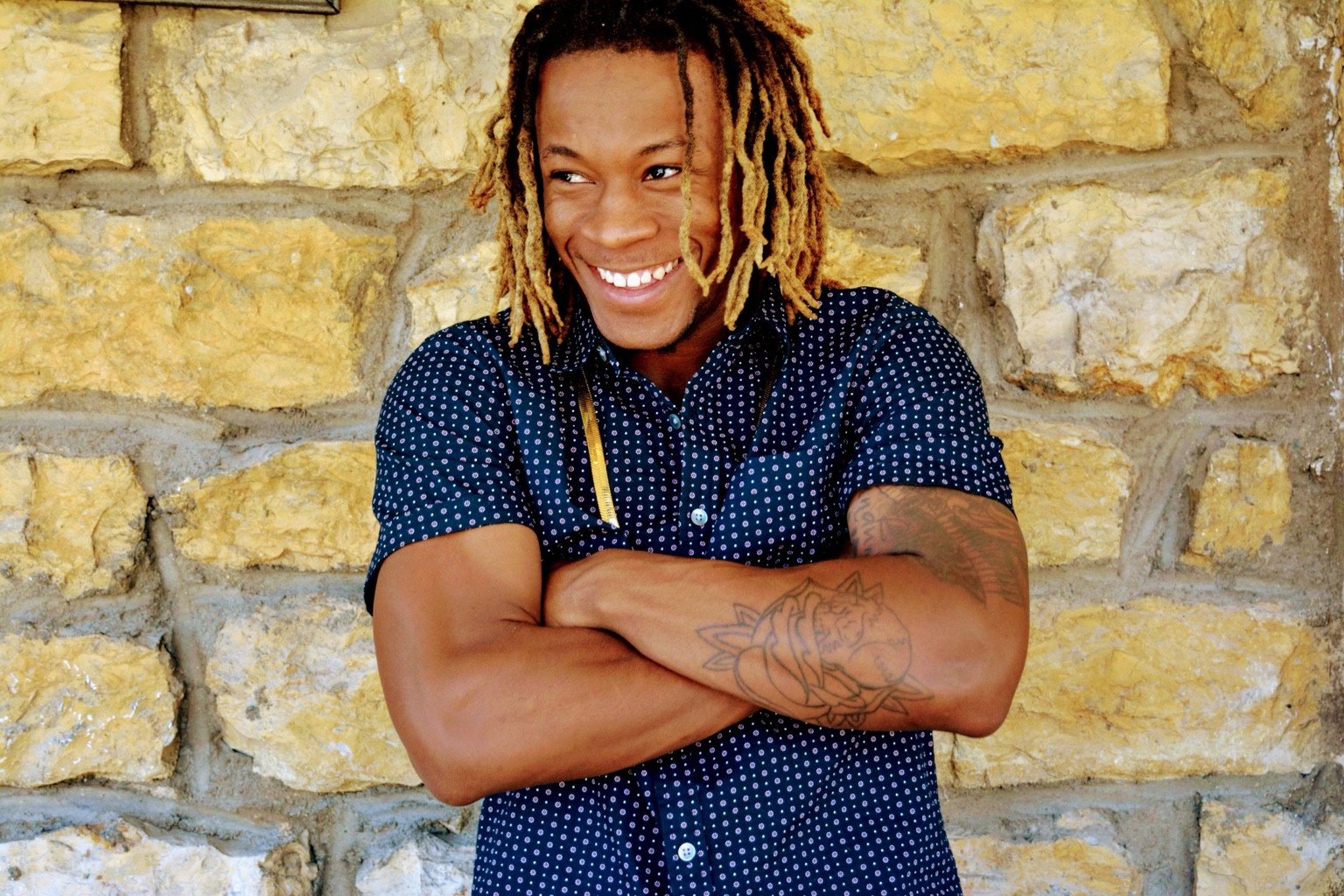 Smiling portrait against a golden stone wall.