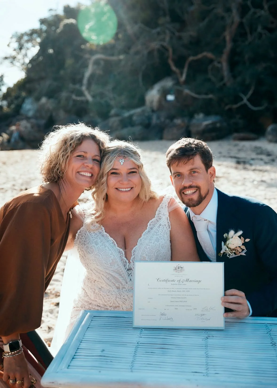 Sydney marriage celebrant Kate Cohen with a happy newlywed couple holding their marriage certificate on Shelly Beach, Manly