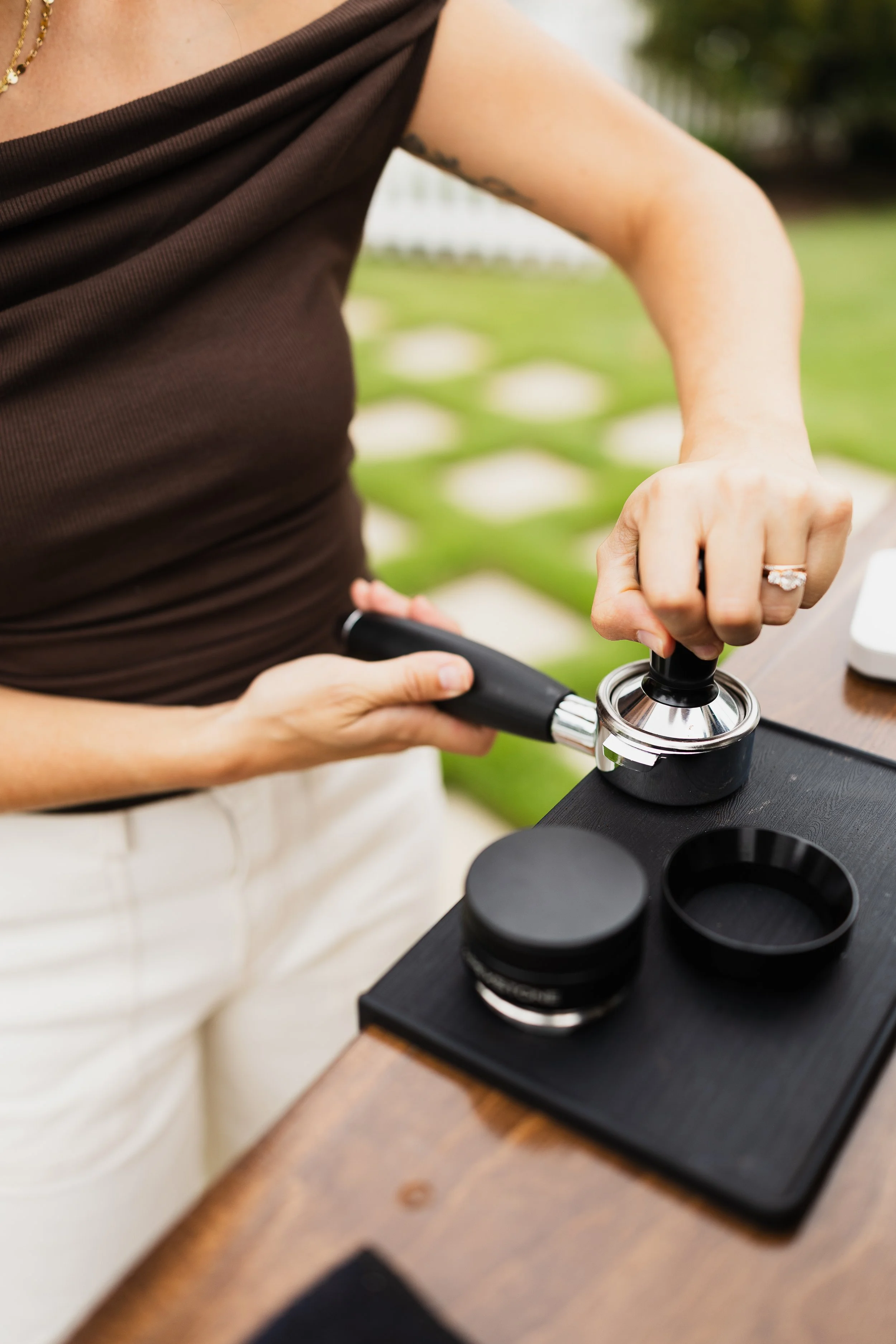 Person wearing a brown top and ring, using a stethoscope on a table with a microscope and sample containers, in an outdoor setting.