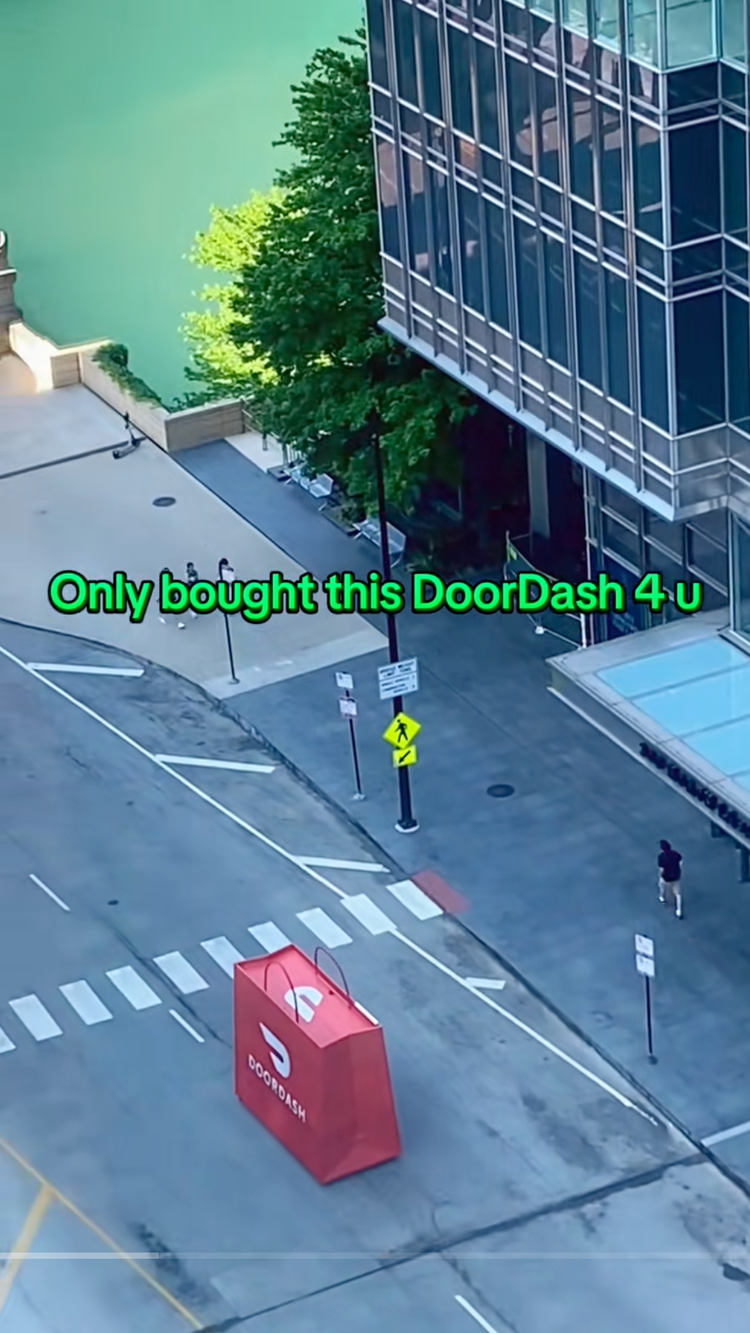 A red DoorDash tent on a city street next to a crosswalk, with a person walking nearby and green text over the image that says "Only bought this DoorDash 4 u."