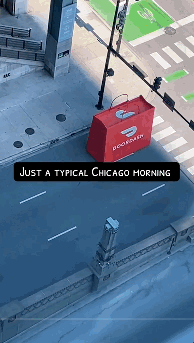 Empty Chicago street with a large red DoorDash delivery bag sitting on the sidewalk near a crosswalk and traffic lights, with no vehicles or pedestrians present.