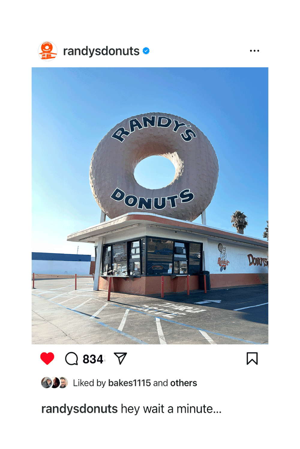 A large, donut-shaped sign reading 'RANDY'S DONUTS' on top of a donut shop with a retro design, clear blue sky, and a parking lot in the foreground.