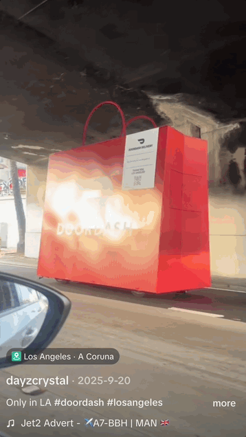 Giant red shopping bag with a white tag hanging under a bridge, advertising DoorDash in Los Angeles.