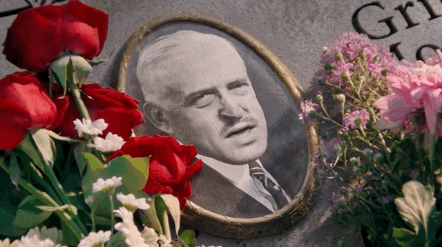 A memorial with red and pink flowers and a framed black and white photo of a man.”}