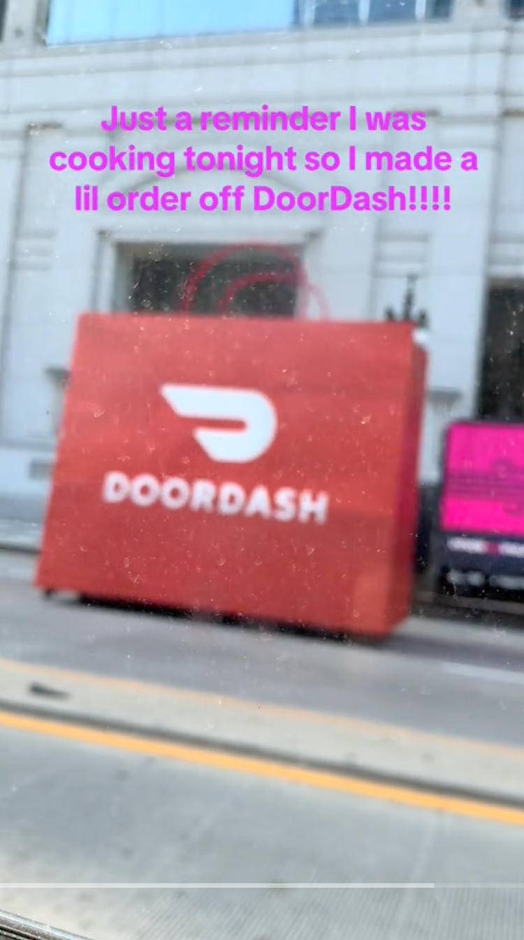 A large red DoorDash delivery bag placed outside a building with a white stone facade. Pink text overlayed on the image reads, "Just a reminder I was cooking tonight so I made a lil order off DoorDash!!!!"