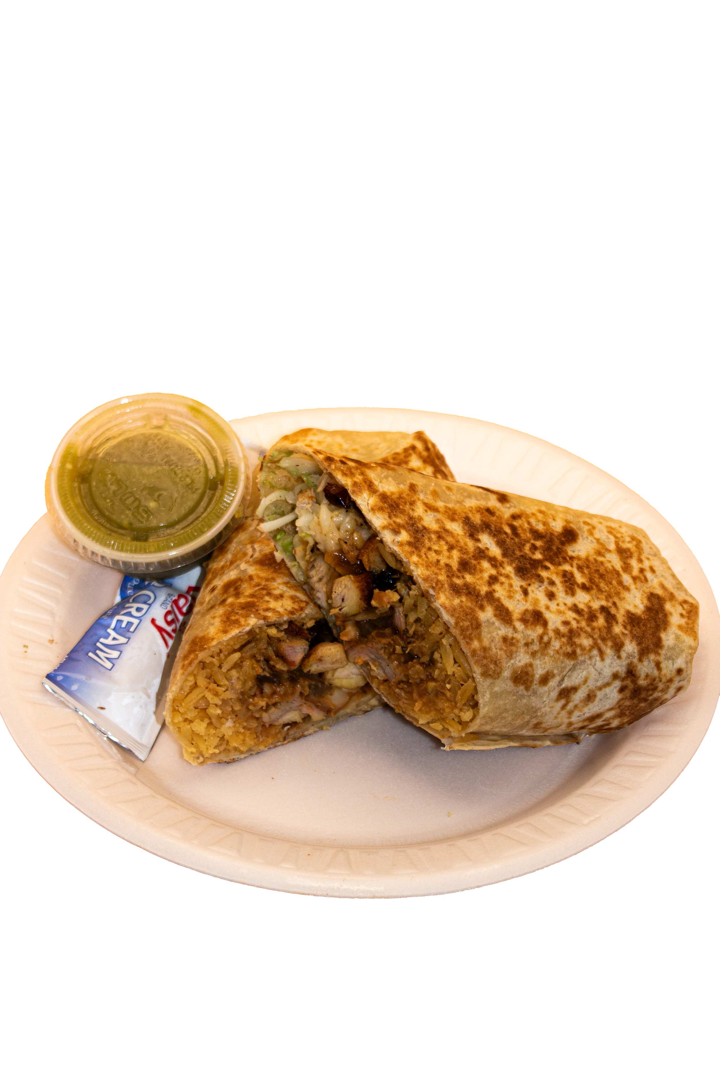 A plate of Mexican food featuring a large burrito cut in half to show rice, beans, chicken, and vegetables inside, with a sealed container of green salsa and a packet of crema on the side.
