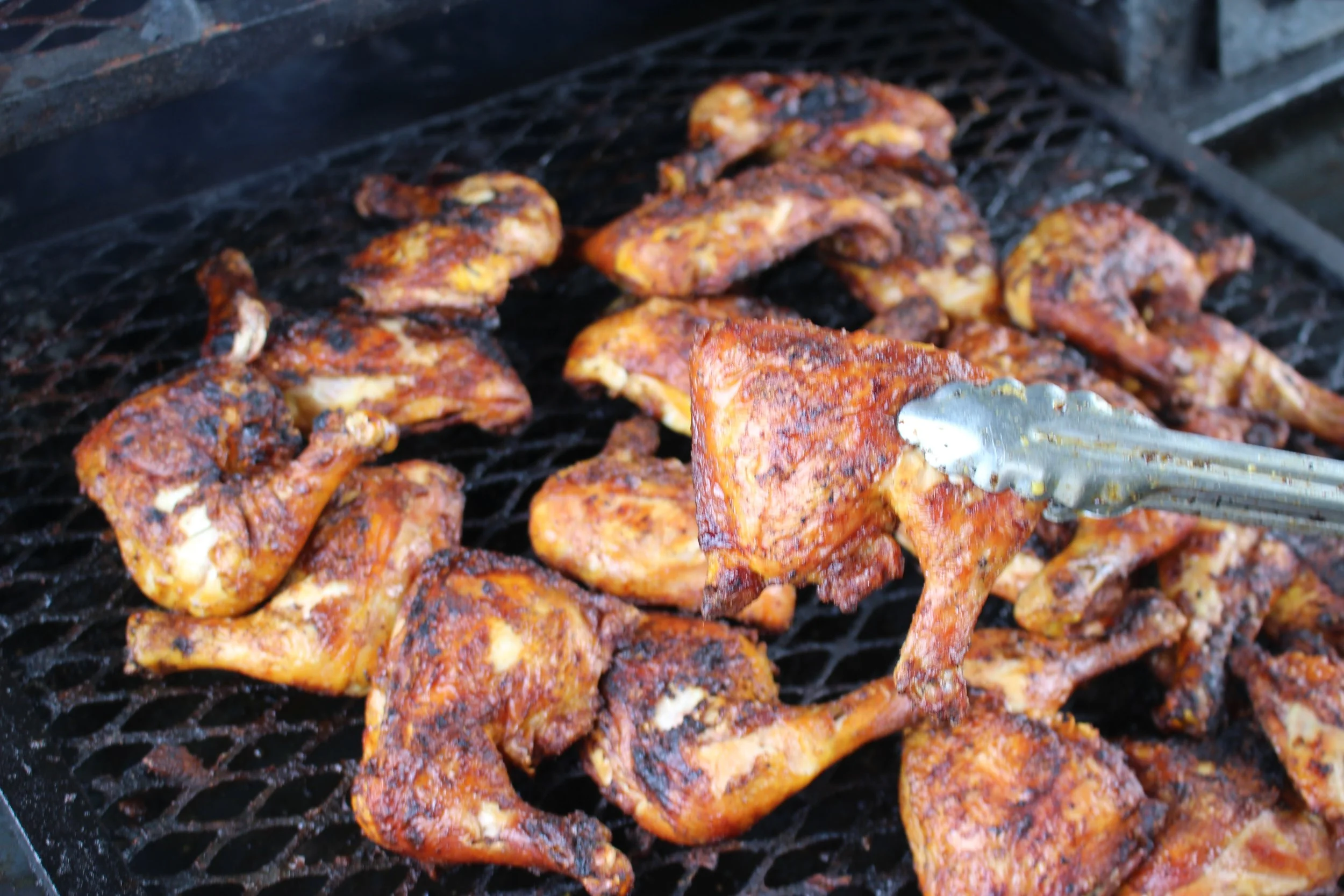 Chicken pieces with spices cooking on a grill, with tongs beside.