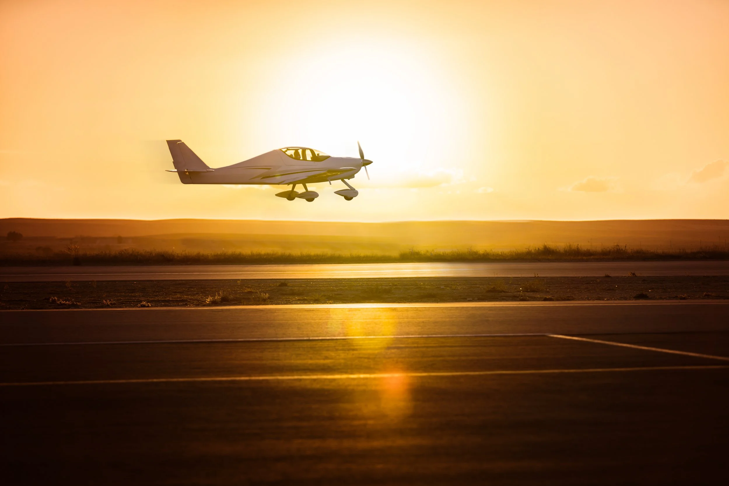 A small airplane flying low over a runway during sunset.