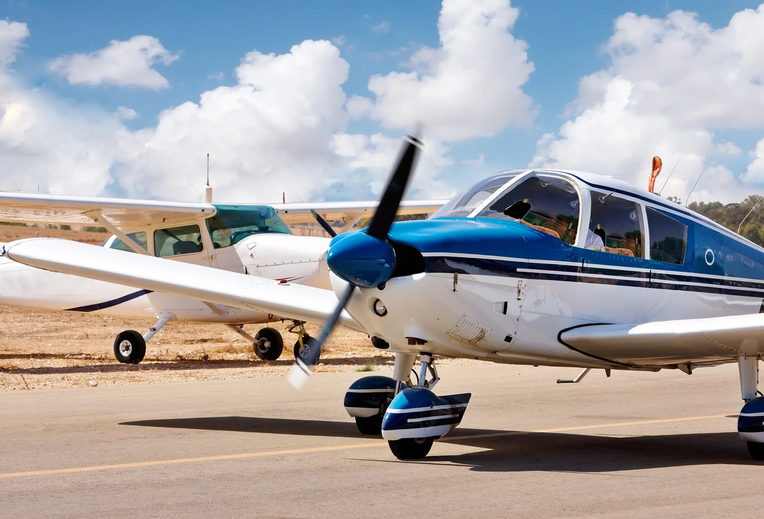Two small passenger airplanes parked on a tarmac under a partly cloudy sky.