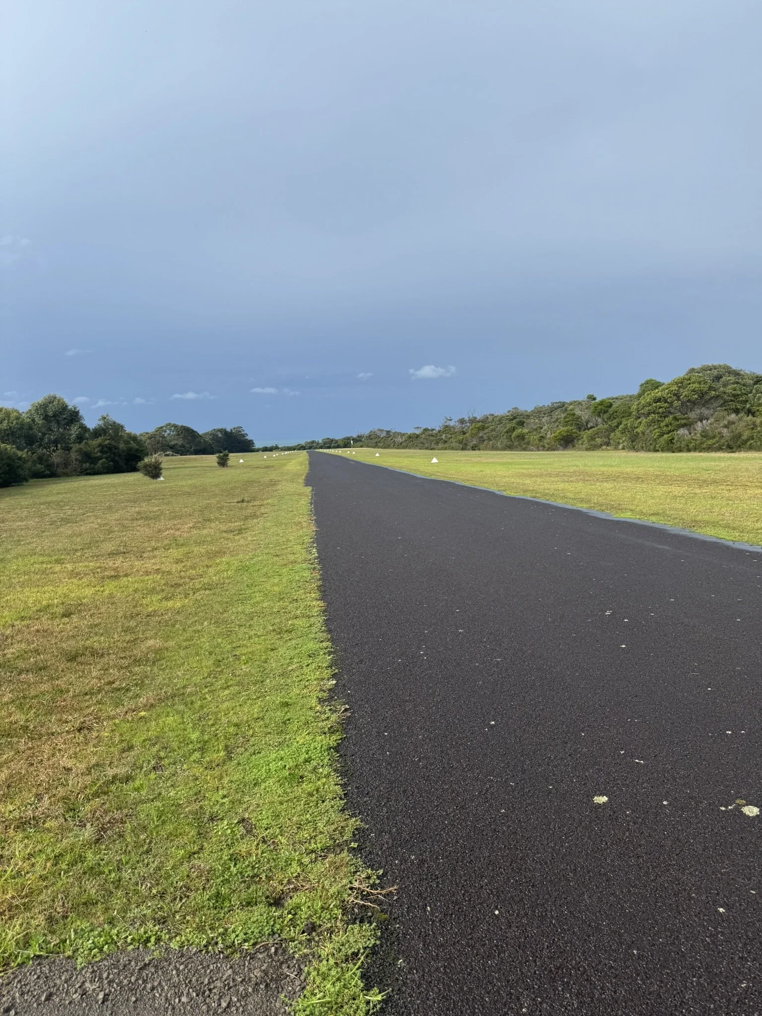 A paved road running through a grassy landscape with trees on either side and a cloudy sky overhead.