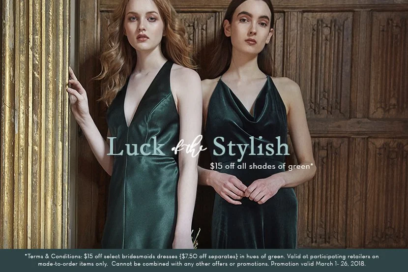 Two women with long hair in satin green dresses standing against a wooden wall, with promotional text offering $15 off on green dresses.