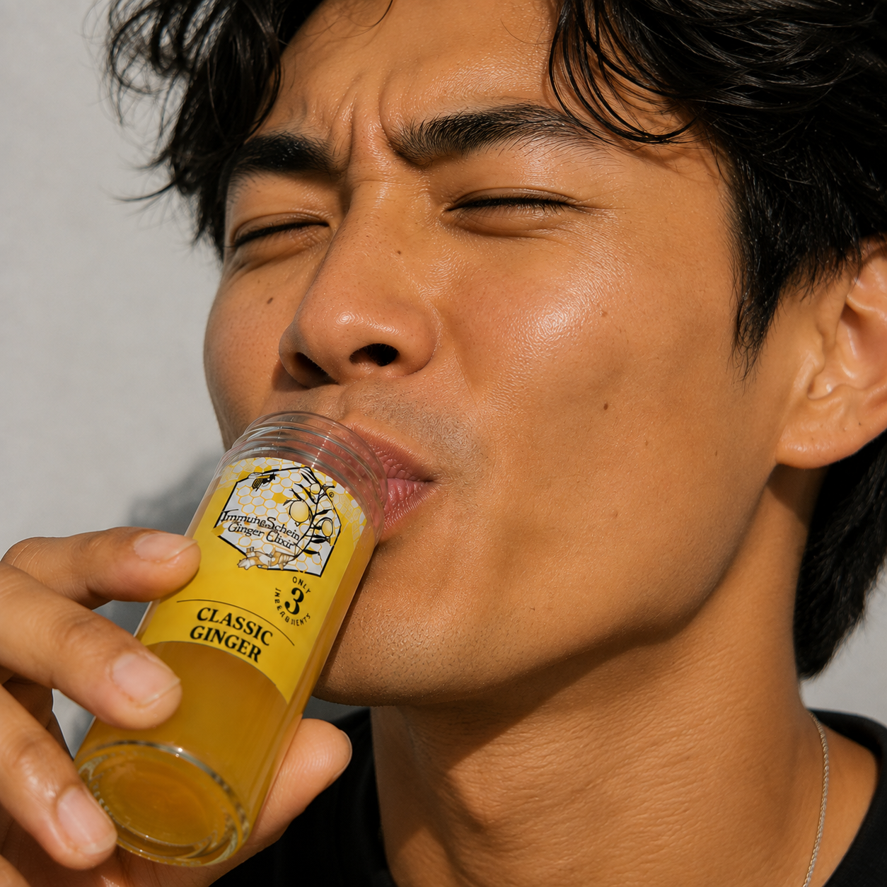 A man with dark hair and tan skin is drinking from a glass labeled 'Classic Ginger' ginger lemonade, with his eyes closed.