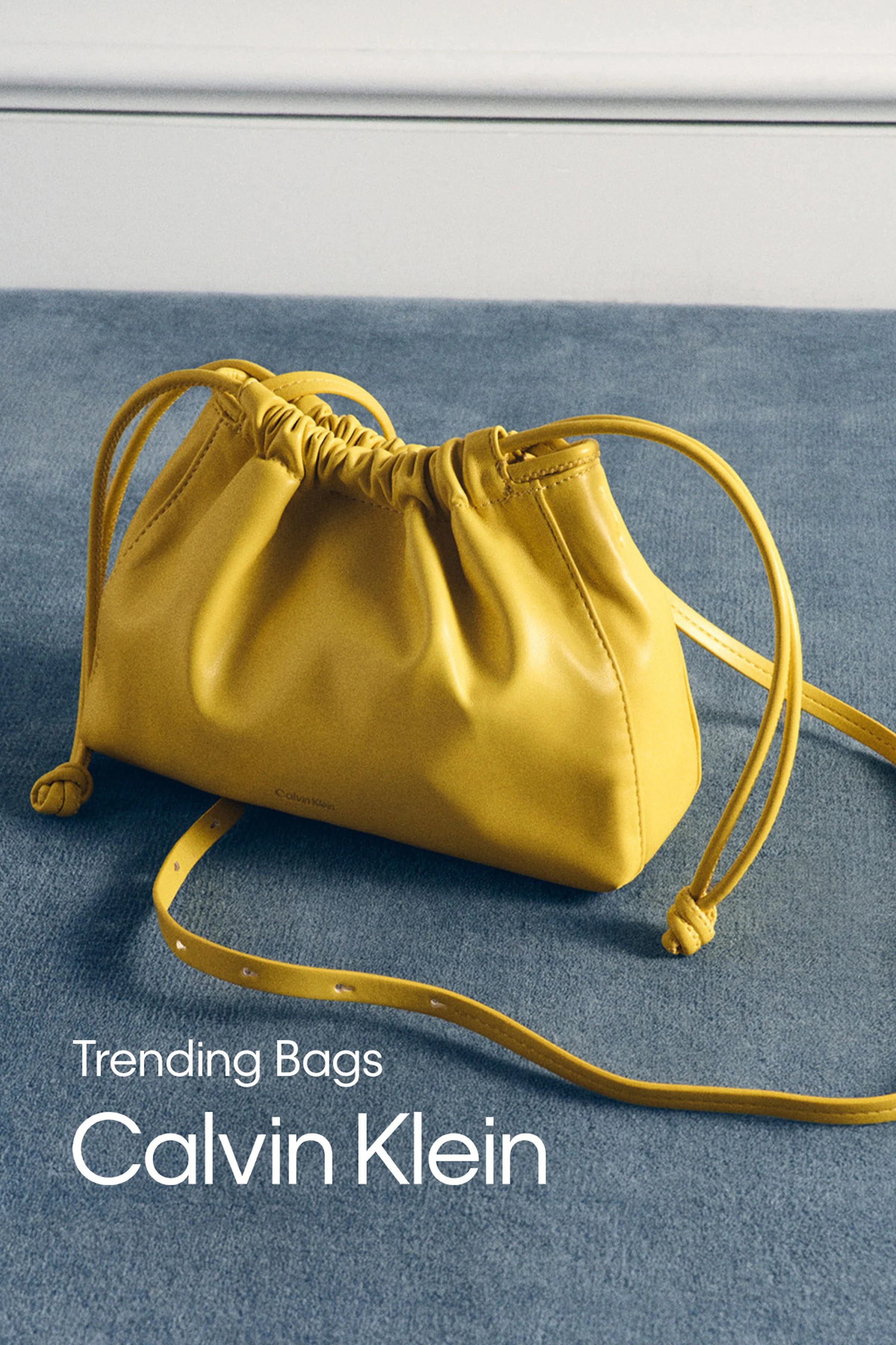 A yellow Calvin Klein handbag on blue fabric with a white wall in the background.