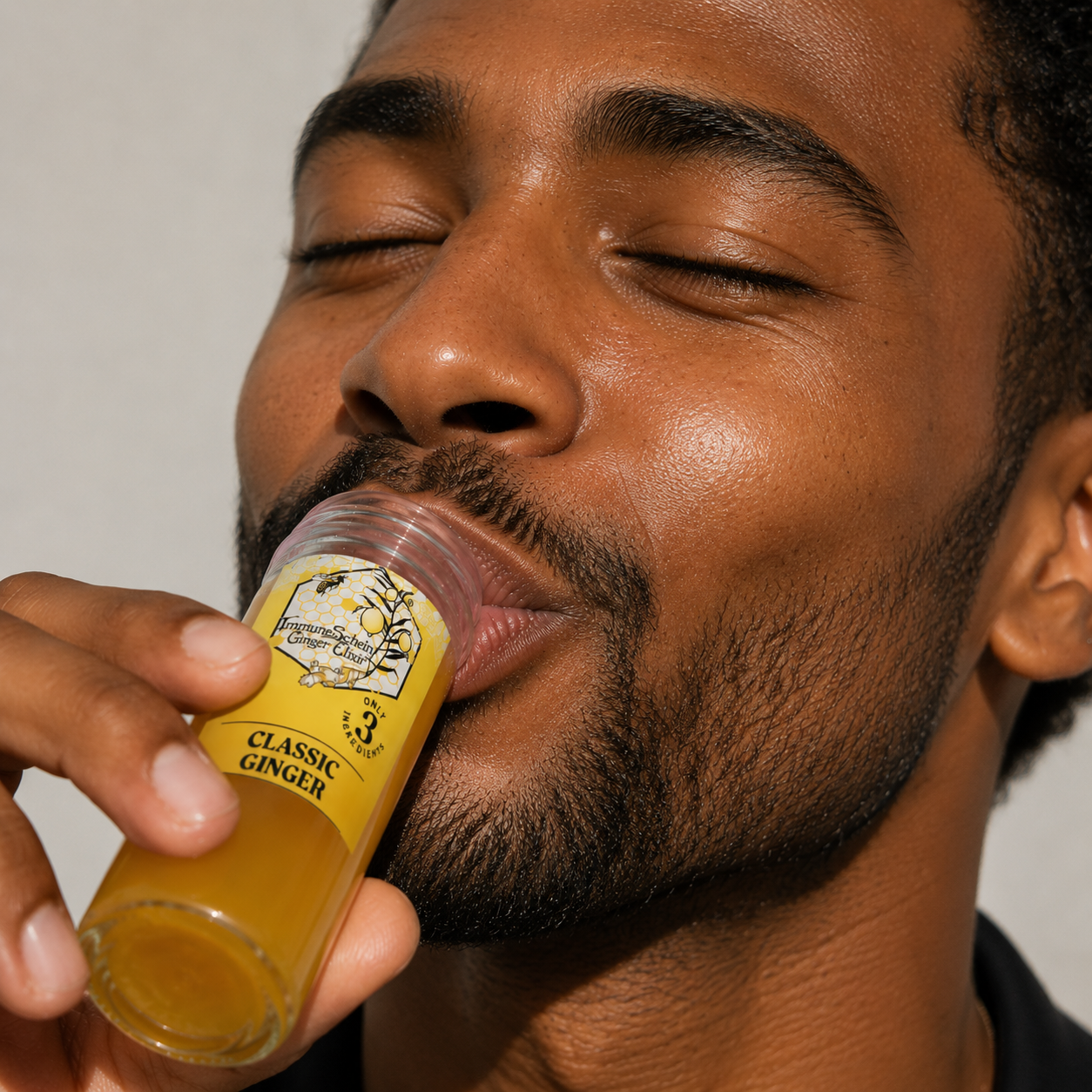 A man with a beard closes his eyes and holds a small glass bottle labeled "Classic Ginger" herbal remedy near his lips, preparing to take a sip.