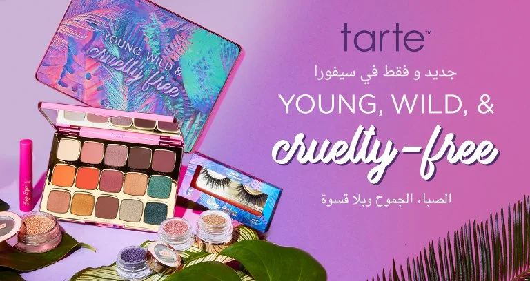 Tarte cosmetics display featuring an eyeshadow palette, false eyelashes, and small containers of glitter, with a purple and pink background and tropical leaf decorations.