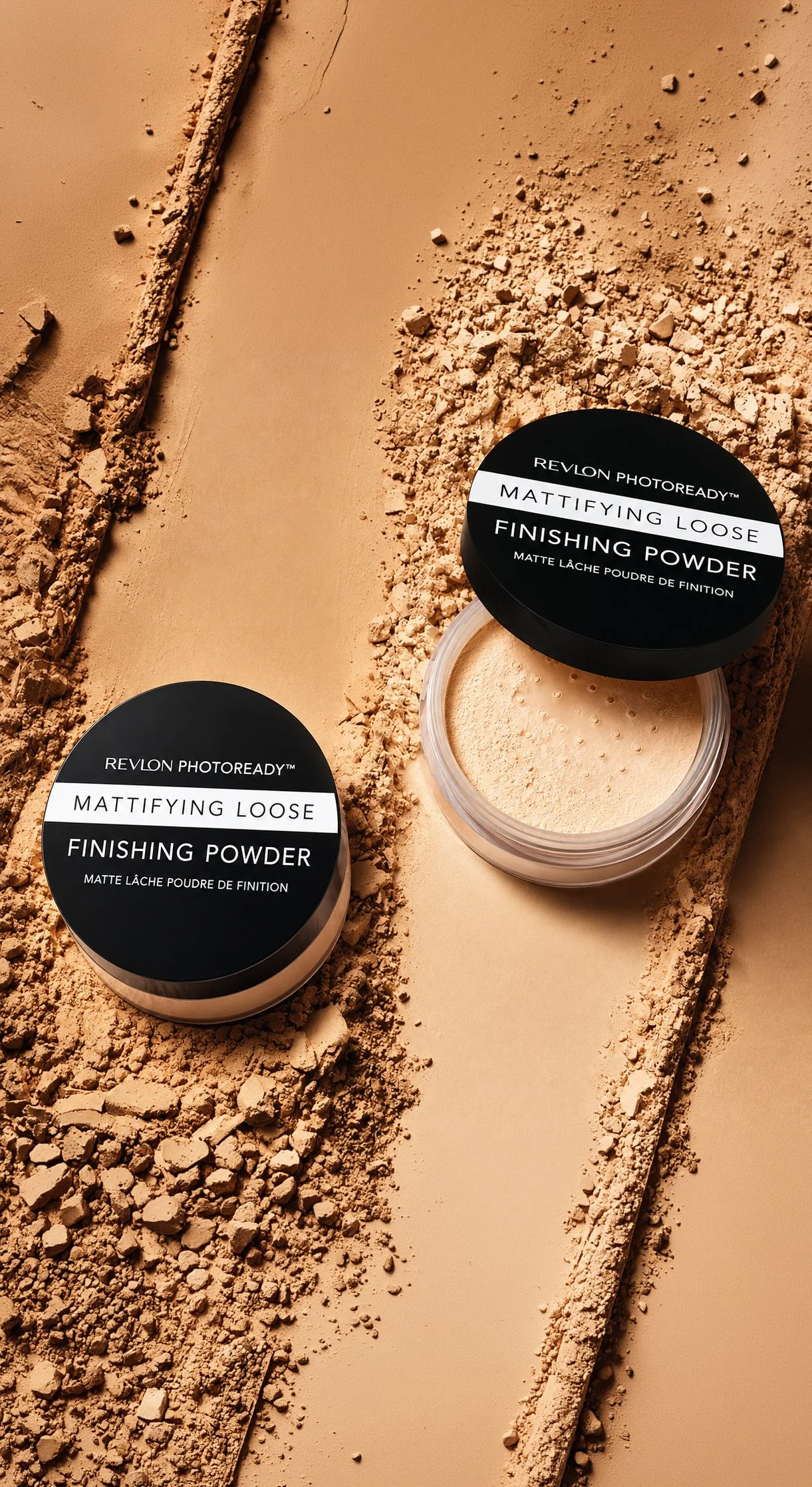 Two open containers of Revlon Photoready Mattifying Loose Finishing Powder on a beige surface with scattered powder and pieces of broken powder.