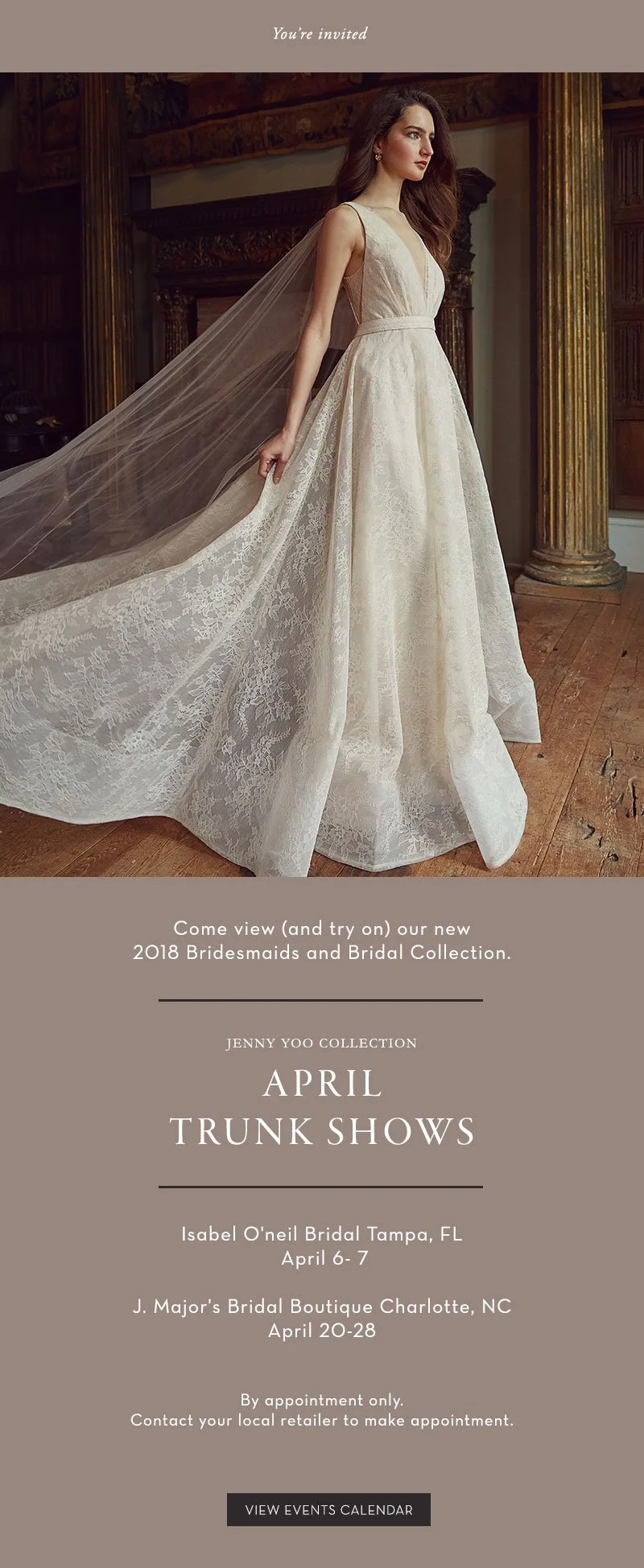 A woman wearing a wedding gown with lace detailing and a long train, standing in an elegant room with wooden floors and ornate pillars, inviting viewers to a bridal trunk show.