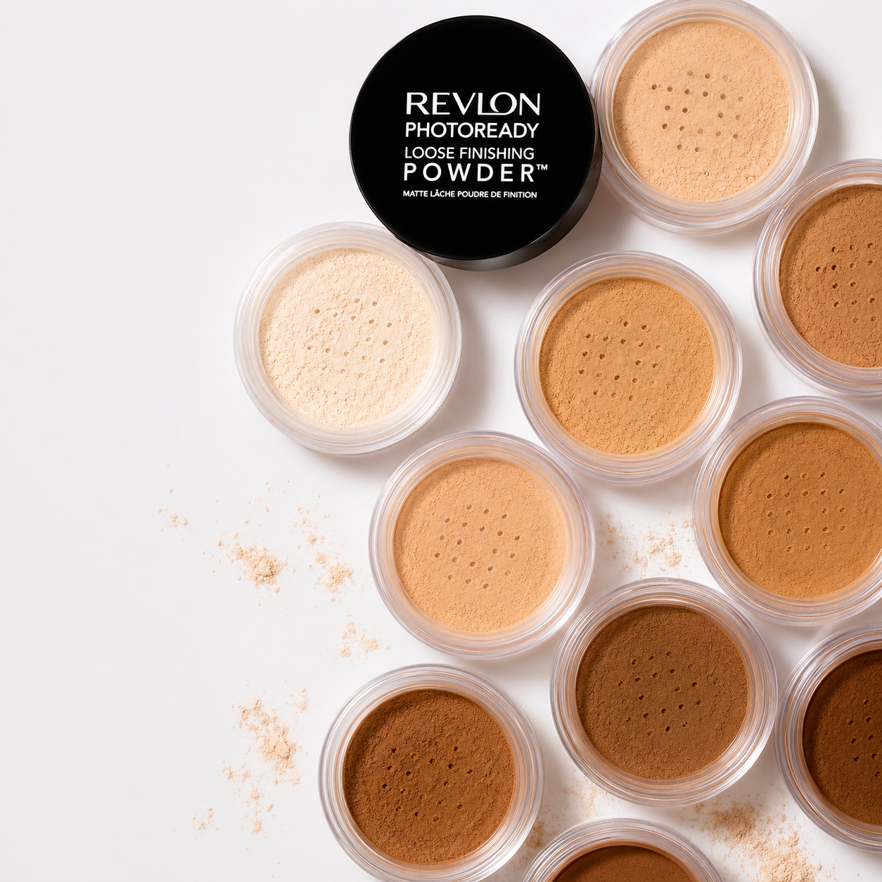 Collection of loose setting powders in small clear containers with a black Revlon Photoready box on a white background.