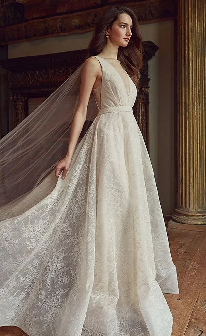 A woman in a white wedding dress with a long train standing in an ornate room with wooden floors and decorative columns.