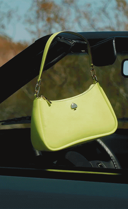 A bright yellow handbag with a small spade emblem hanging on the rearview mirror of a car.