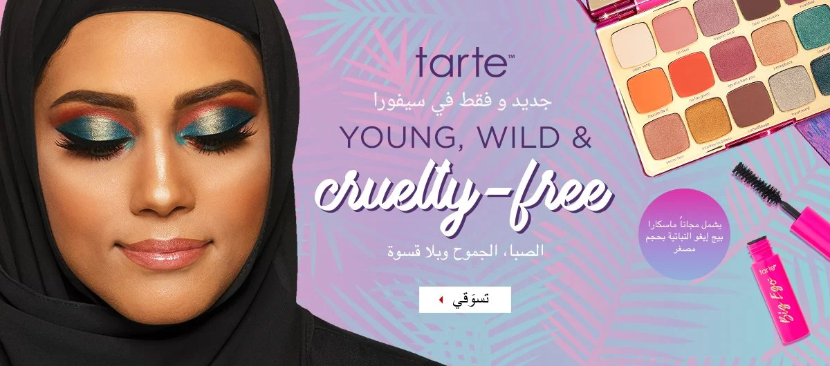 A woman with makeup featuring bold blue eyeshadow and pink lipstick, wearing a black hijab. To the right, there is a colorful eyeshadow palette and a pink mascara with a brush. The background includes purple and blue tropical leaf patterns, and Arabic and English text promoting cruelty-free, young, wild makeup products from Tarte.