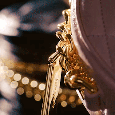 Close-up of a gold chain and clasp attached to a purple purse with blurred bokeh lights in the background.