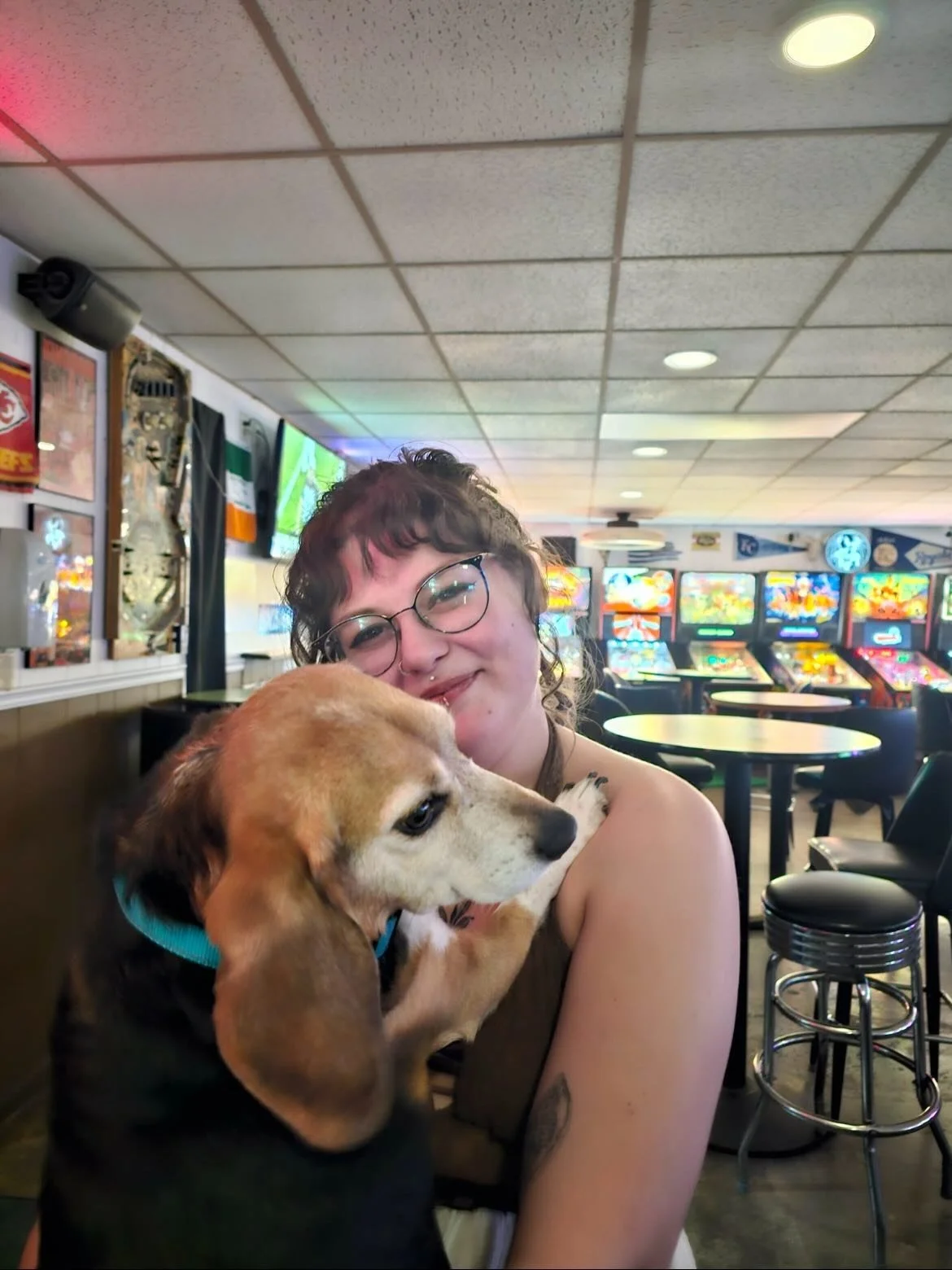 Guest holding a dog inside 403 Club with bright bar lighting and arcade ambiance in Strawberry Hill, Kansas City